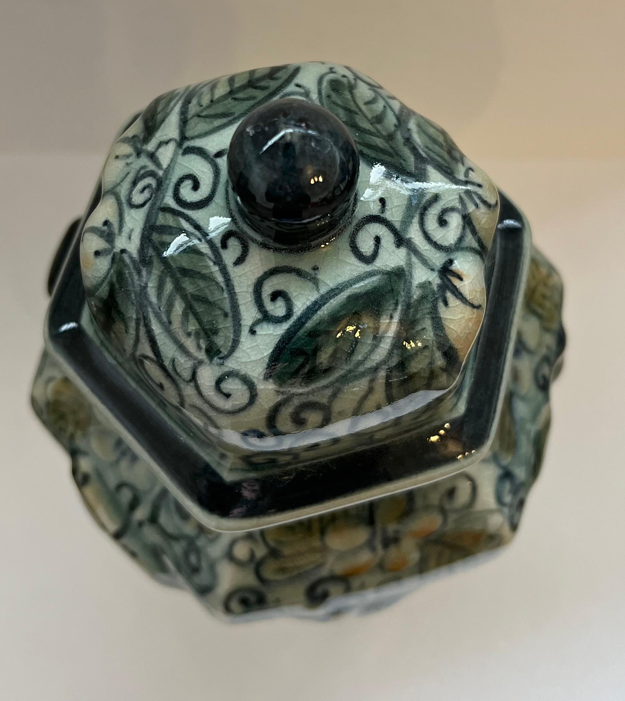 Stunning Maitland Smith Celadon Ceramic Crackle Covered Jar that was handmade in Thailand. It has a vibrant, hand-painted floral and leaf motif with raised ornate designs on each of its six sides. The vase has a subtle crackle glaze and ornate