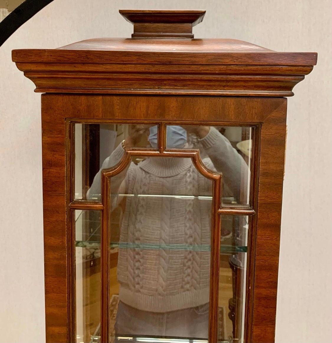 Maitland Smith Chinese Chippendale style cabinet has a pagoda shaped top surmounting the one glass door case with latticework over the two-drawer over one door that opens to storage. Glass door opens to two thick glass shelves to display your