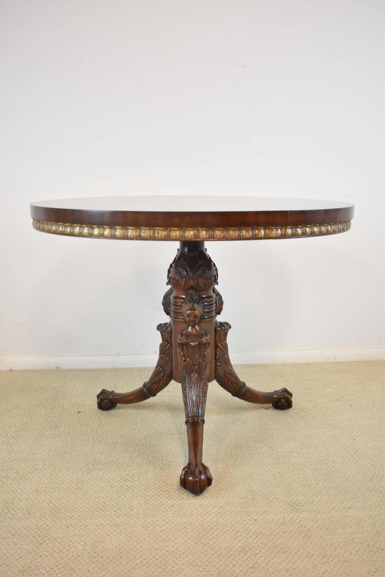 An elegant round center table by Maitland Smith. Mahogany with a hand-carved tripod base that features female figures and ball and claw feet. The round burled top has a gold gilt banding around the edge. This table is in beautiful condition.