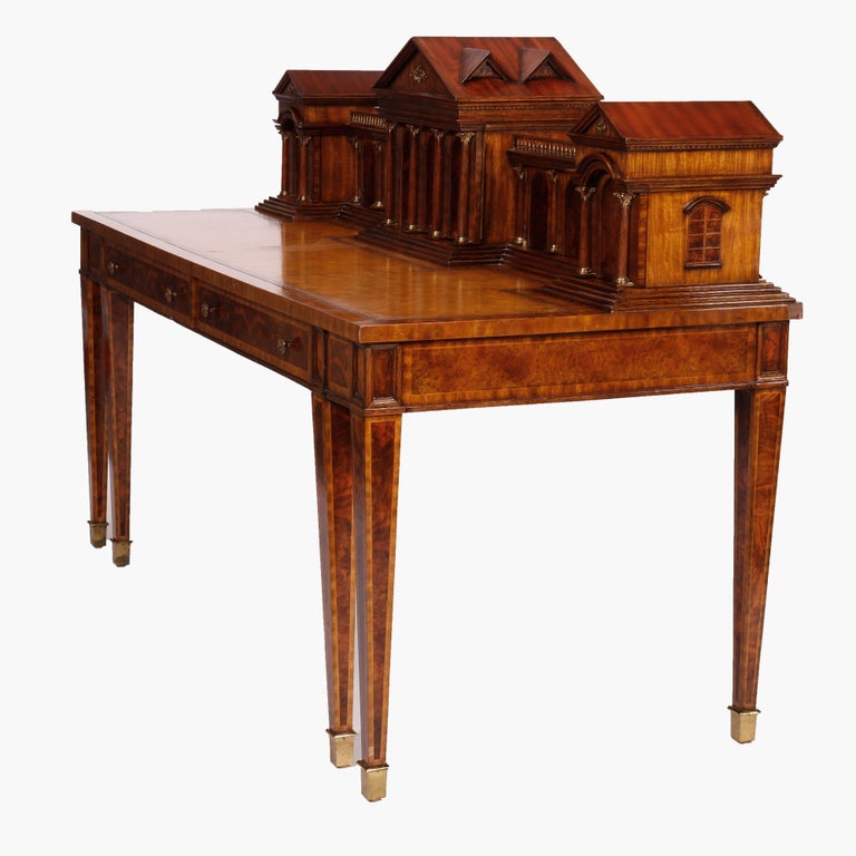 An executive desk by Maitland Smith offers mahogany construction in Classical Romanesque form with architectural splash having satinwood inlay detailing throughout over gilt decorated leather writing surface and raised on straight and tapered banded