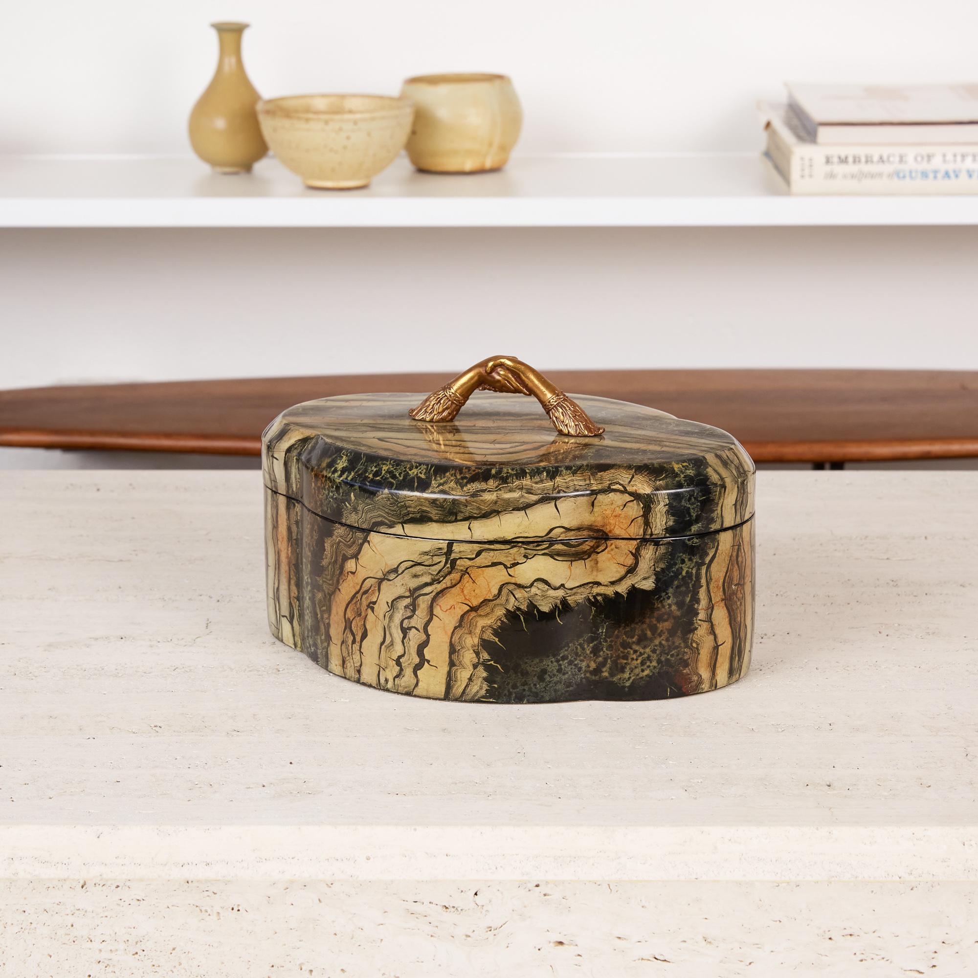 Maitland Smith decorative box, circa 1970s. The box features a hand painted petrified wood style exterior with black lacquered interior. The top is accented by a brass handle made of two arms with shaking hands. The chic design is the perfect piece