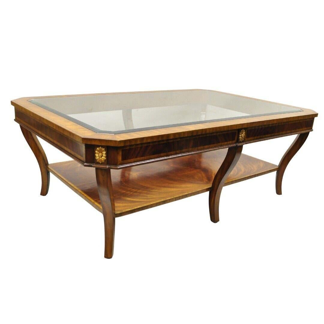 Maitland Smith Empire Style Large Banded Inlay Mahogany Glass Top Coffee Table. Item features beveled glass, inset top, 6 saber legs, 2 tier banded and inlayed crotch mahogany frame, original label, large impressive size. Circa Late 20th Century.