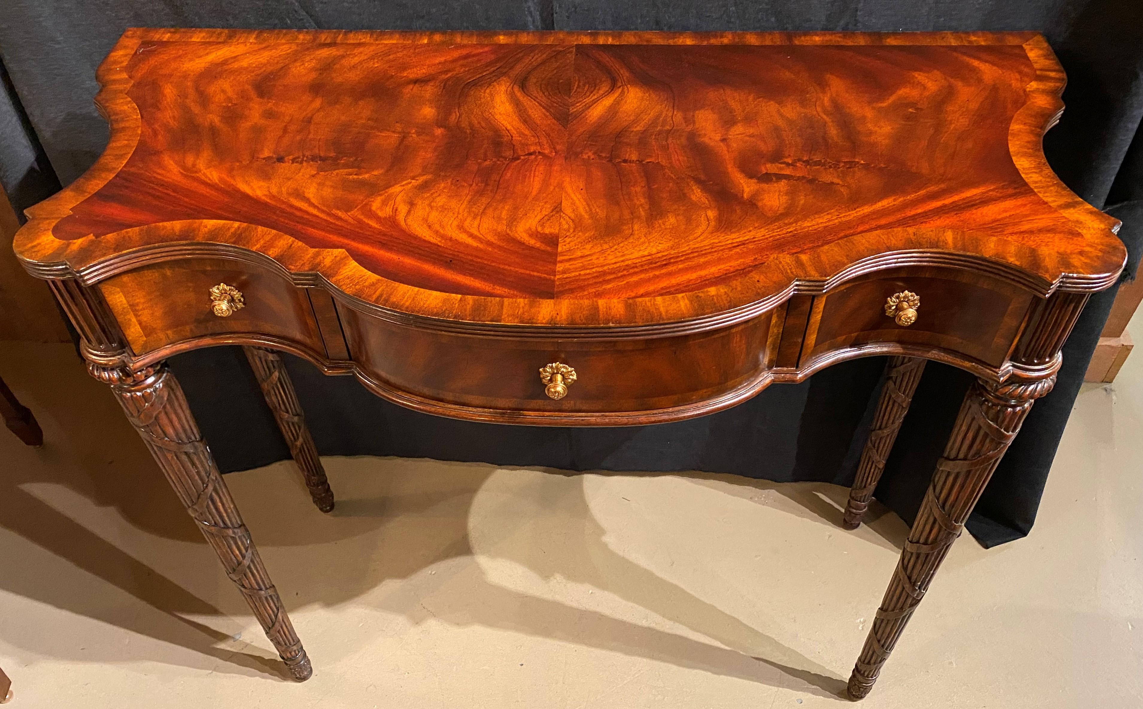 A beautiful three-drawer pier or console table in flame mahogany veneer by Maitland-Smith, with conforming cross-banded top surmounting a frieze with center drawer flanked by two fitted drawers, each with brass pulls and crossbanded drawer fronts,