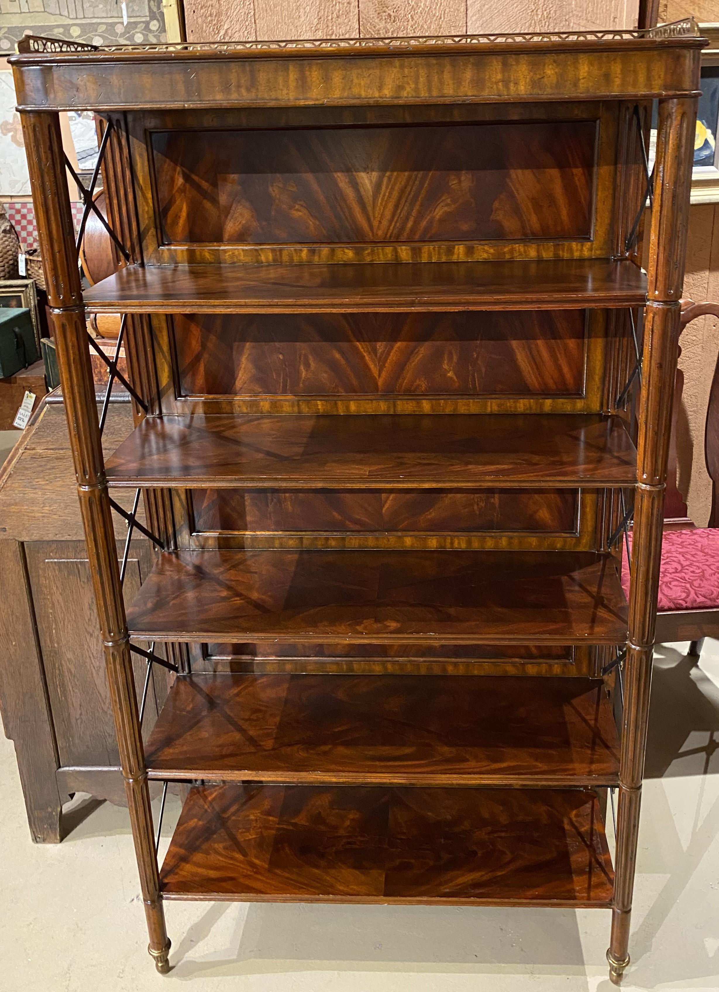 A fine Maitland Smith étagère or bookcase with five shelves, book matched flame mahogany back veneers with crossbanded borders, small top brass gallery, ebonized metal cross shelf end supports with brass rosettes, reeded front corner legs with brass