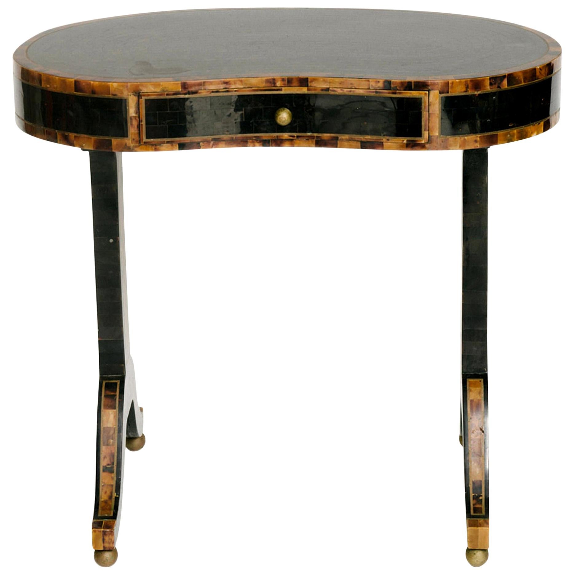 A wonderful Maitland-Smith kidney shaped occasional table with mix of ebony and tortoise colored horn veneers. This table features a single drawer, brass inlay detail and brass ball accents.