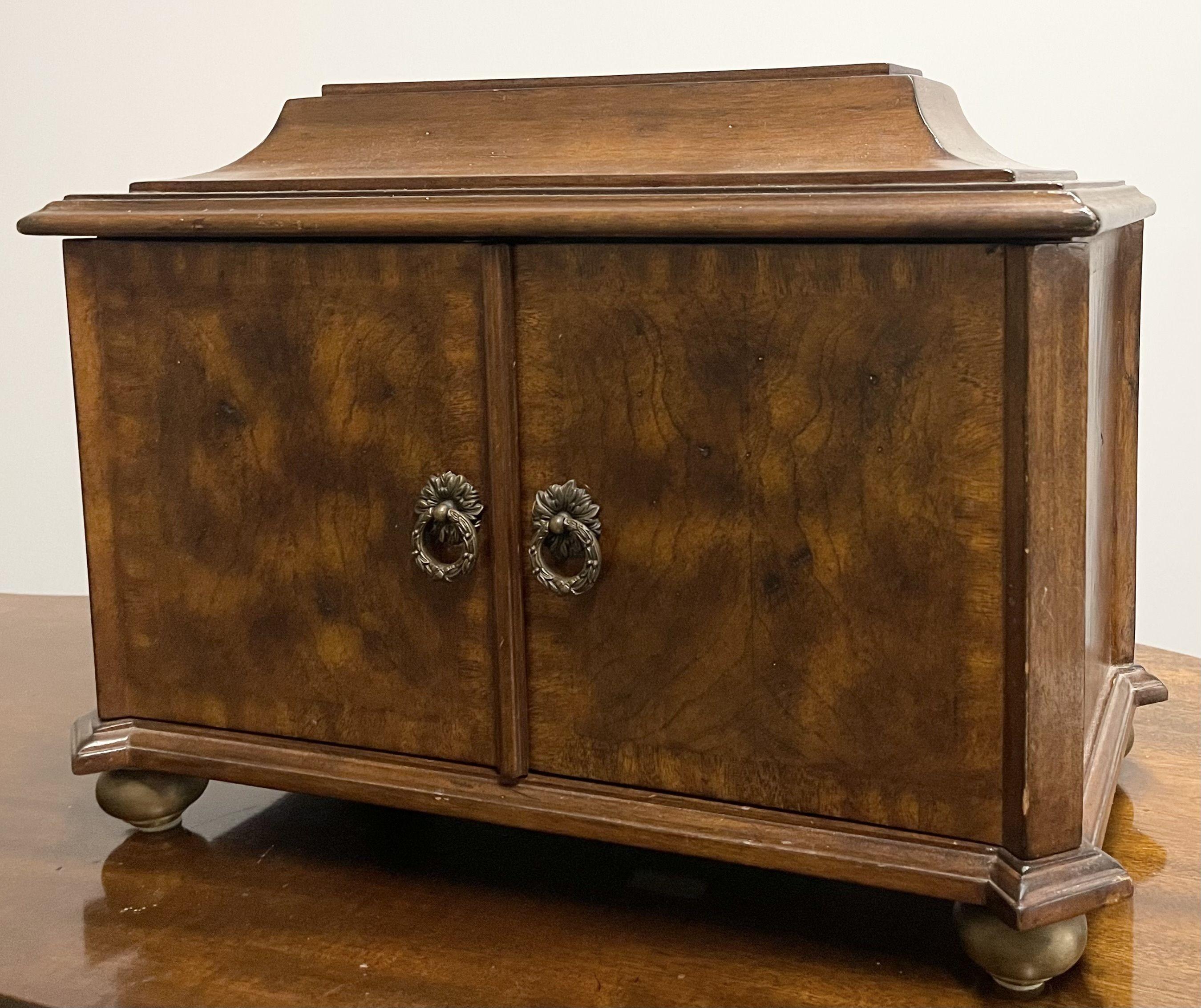 A Detailed Maitland Smith Jewelry Box of Fine Form having Brass Feet and a fully velour lined interior. The outer casket box having two center doors that open and lead to a group of small drawers flanking a center pop open door. The exterior of burl