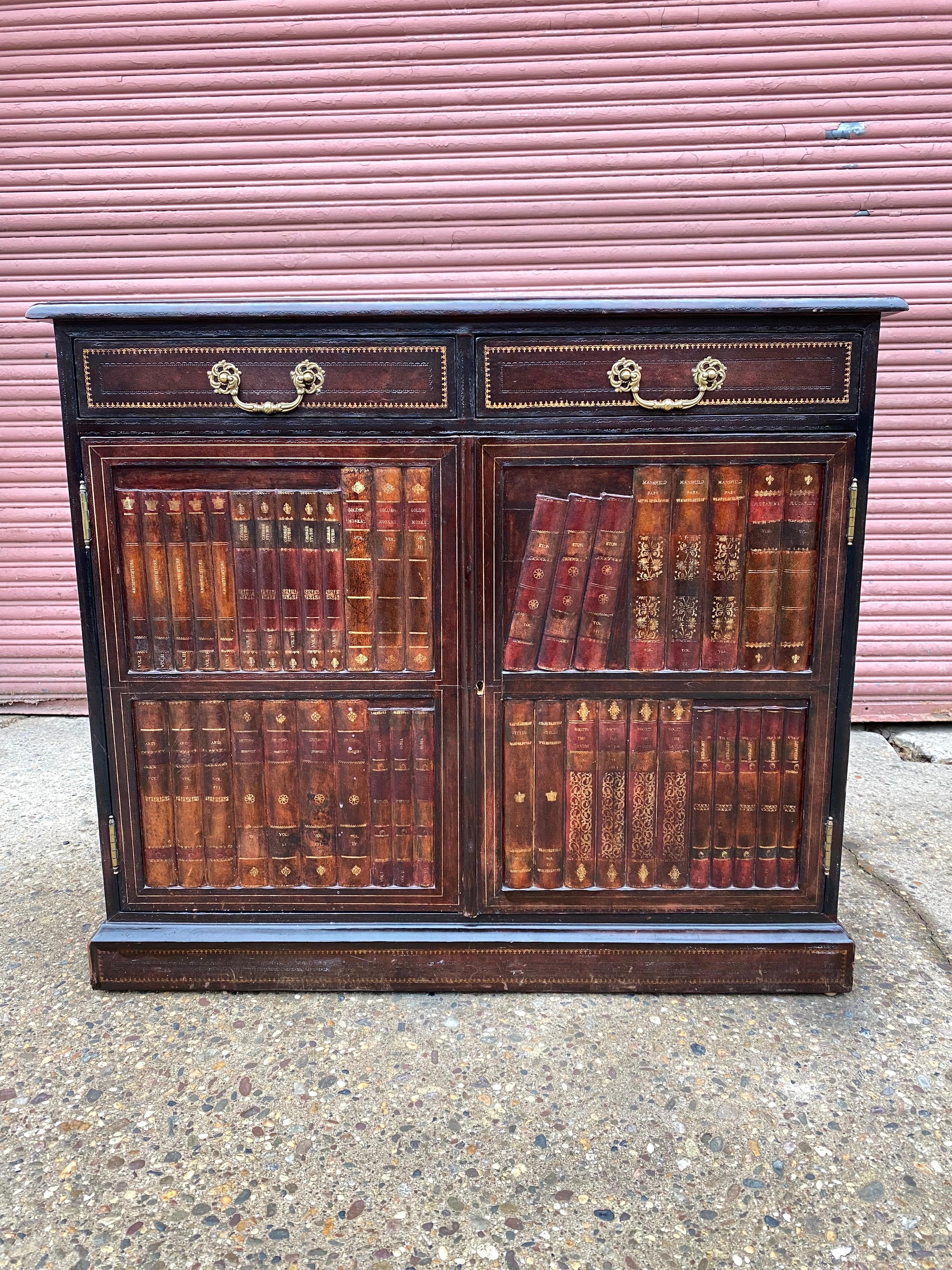 Maitland Smith leather faux bookcase 2 door cabinet with 2 pull out drawers. Clever Design with raised book spines and leaning books. Very nice condition! Great Scale and size, only 14.5 deep! Perfect for shallow spots. Brass handles, one adjustable