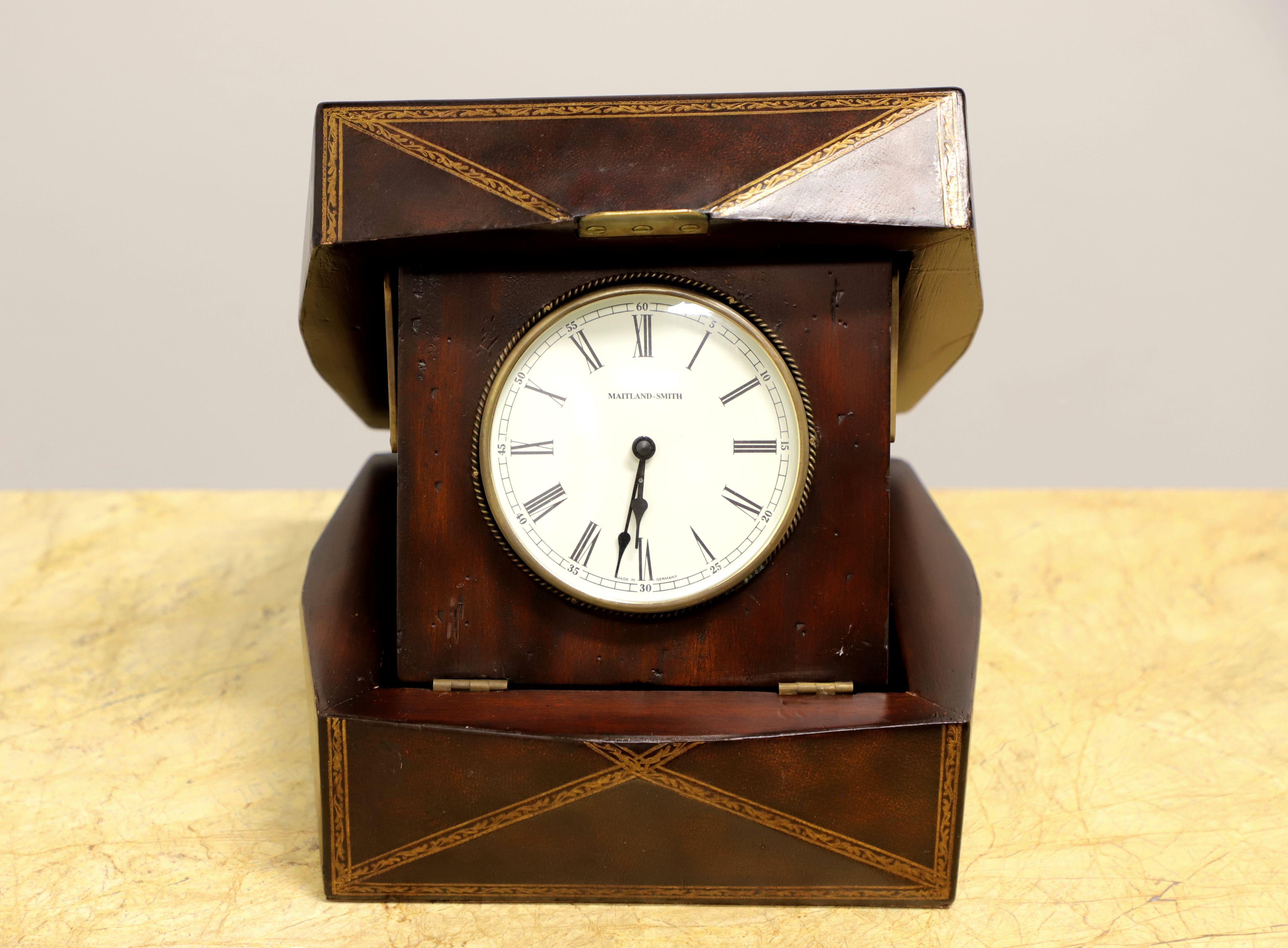 A decorative desk top clock in a leather clad box by Maitland Smith. Mahogany box, leather clad and gold embossed. German made, battery operated, clock set into mahogany on hinges to face prominently when box is opened. Round glass covered clock