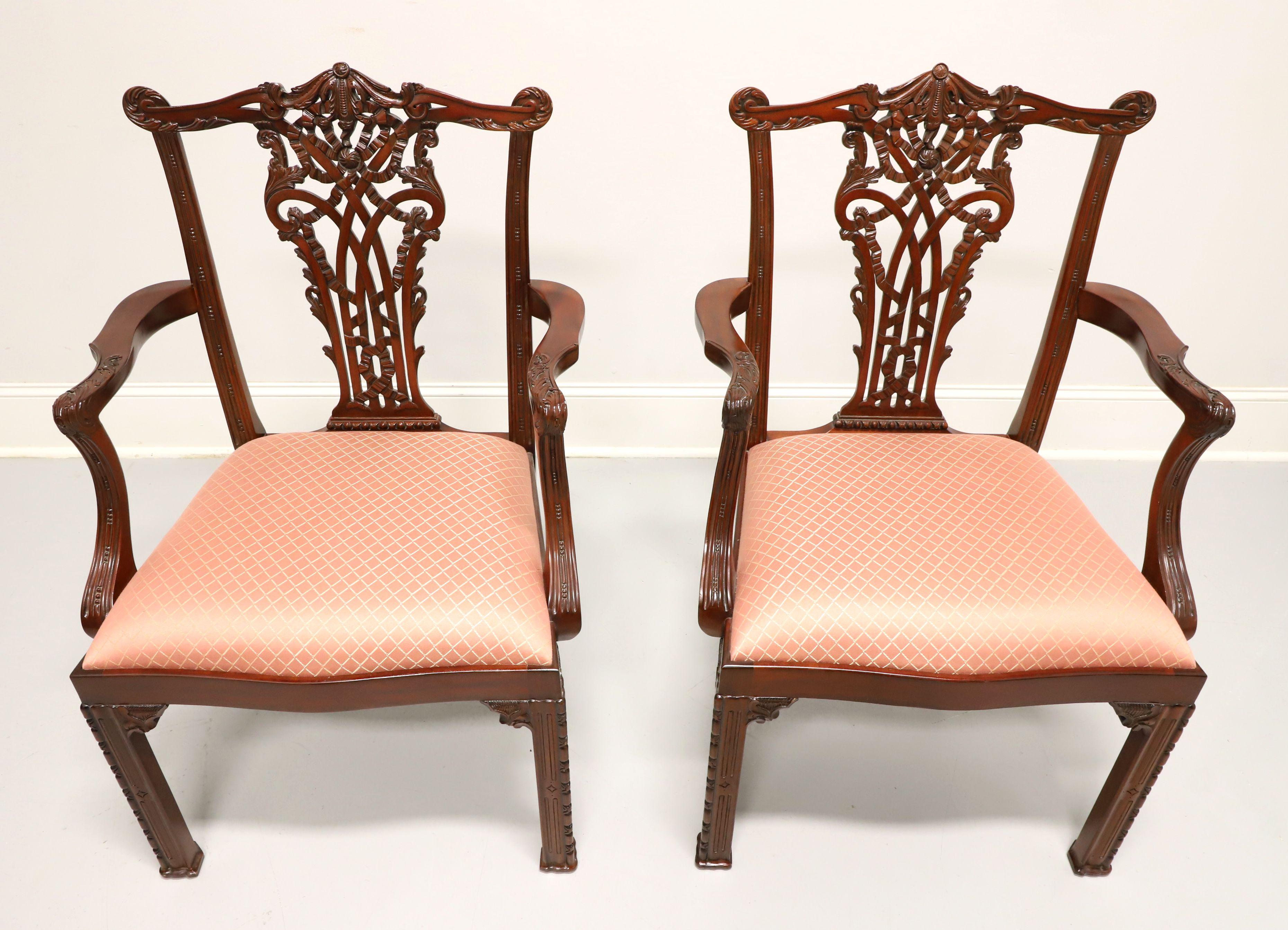 A pair of Chinese Chippendale style dining armchairs by Maitland Smith. Solid mahogany with carved crest rail, backrest, curved carved arms, and decorative fretwork details to straight front legs. Seats are upholstered in a salmon colored diamond