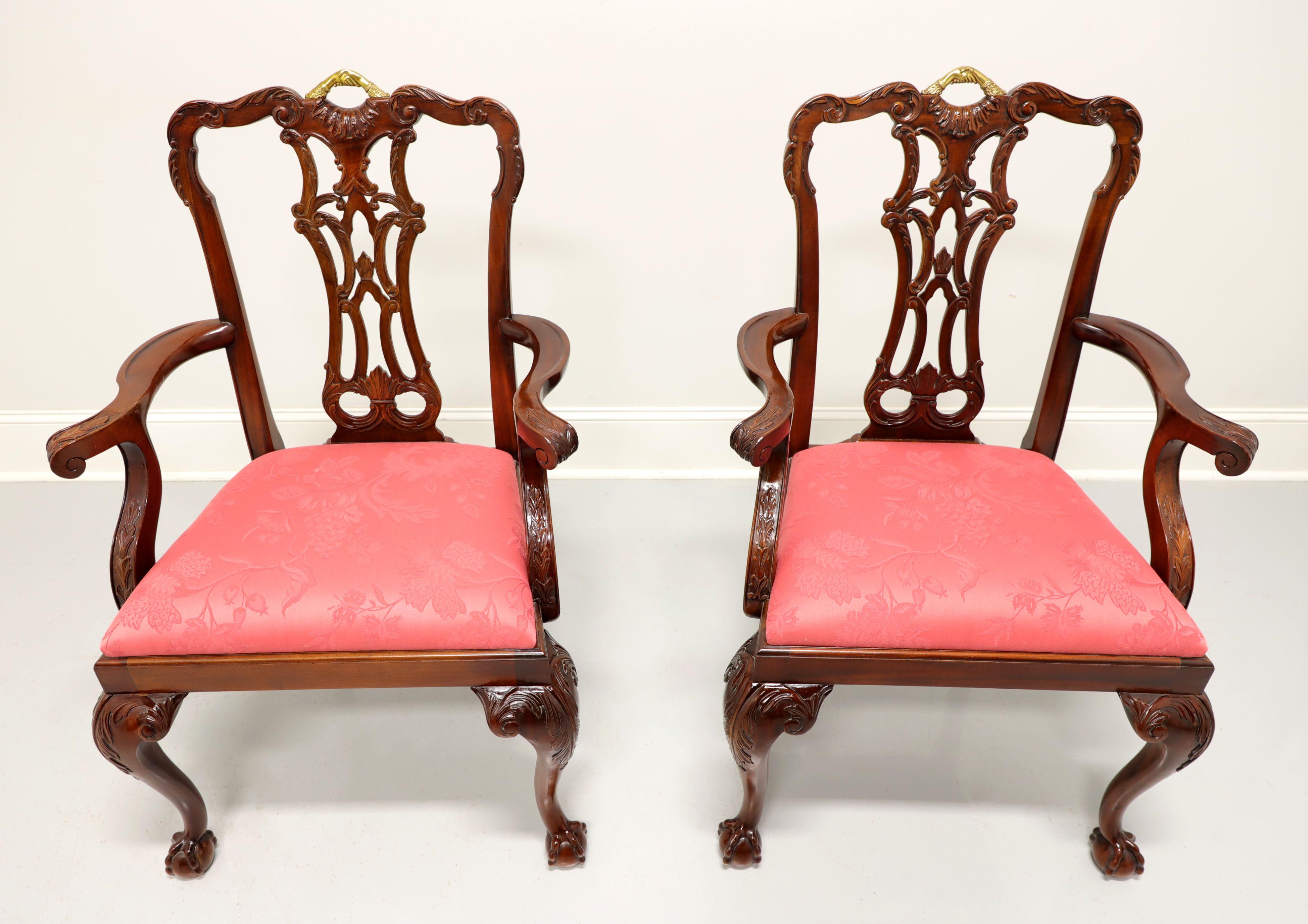 A pair of Chippendale style dining armchairs by Maitland Smith. Solid mahogany with carved crest rails, gold painted handle on top, carved backs, rose color brocade like fabric upholstered seats, carved acanthus leaf to knees, curved legs and ball