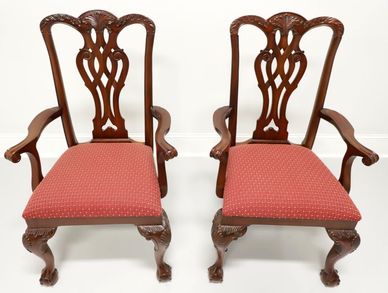 A pair of Georgian style dining armchairs by Maitland Smith. Solid mahogany with carved crest rails, carved back rests, carved curved arms, red & gold color fabric upholstered seats, carved fan to knees, curved legs and ball in claw feet. Made in