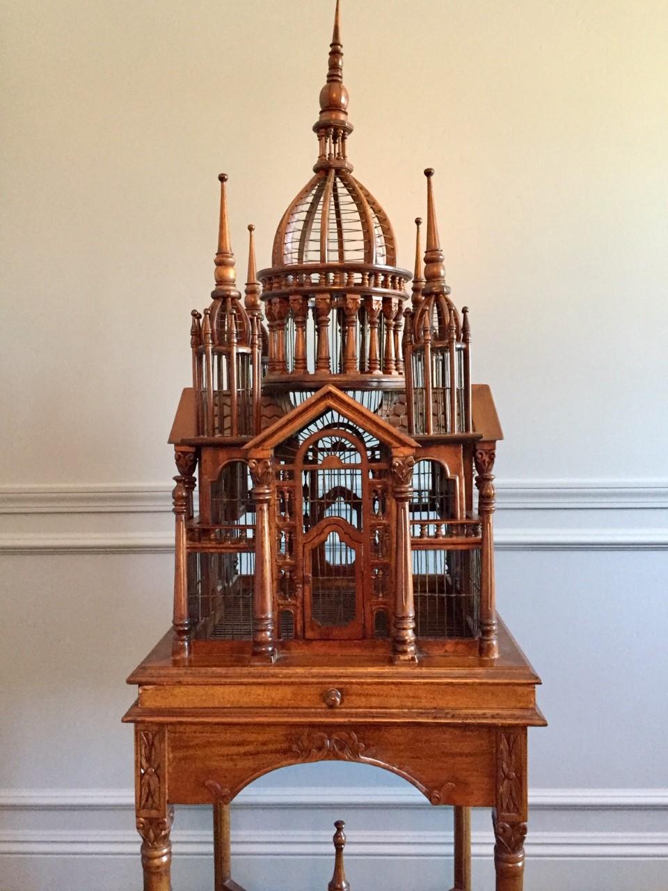 Rare Maitland Smith architectural bird cage on stand featuring hand carved mahogany Victorian style palatial structure with a porticoed temple and spires on the tops. Mounted on a square table with elegant tapered legs and a carved apron and slide