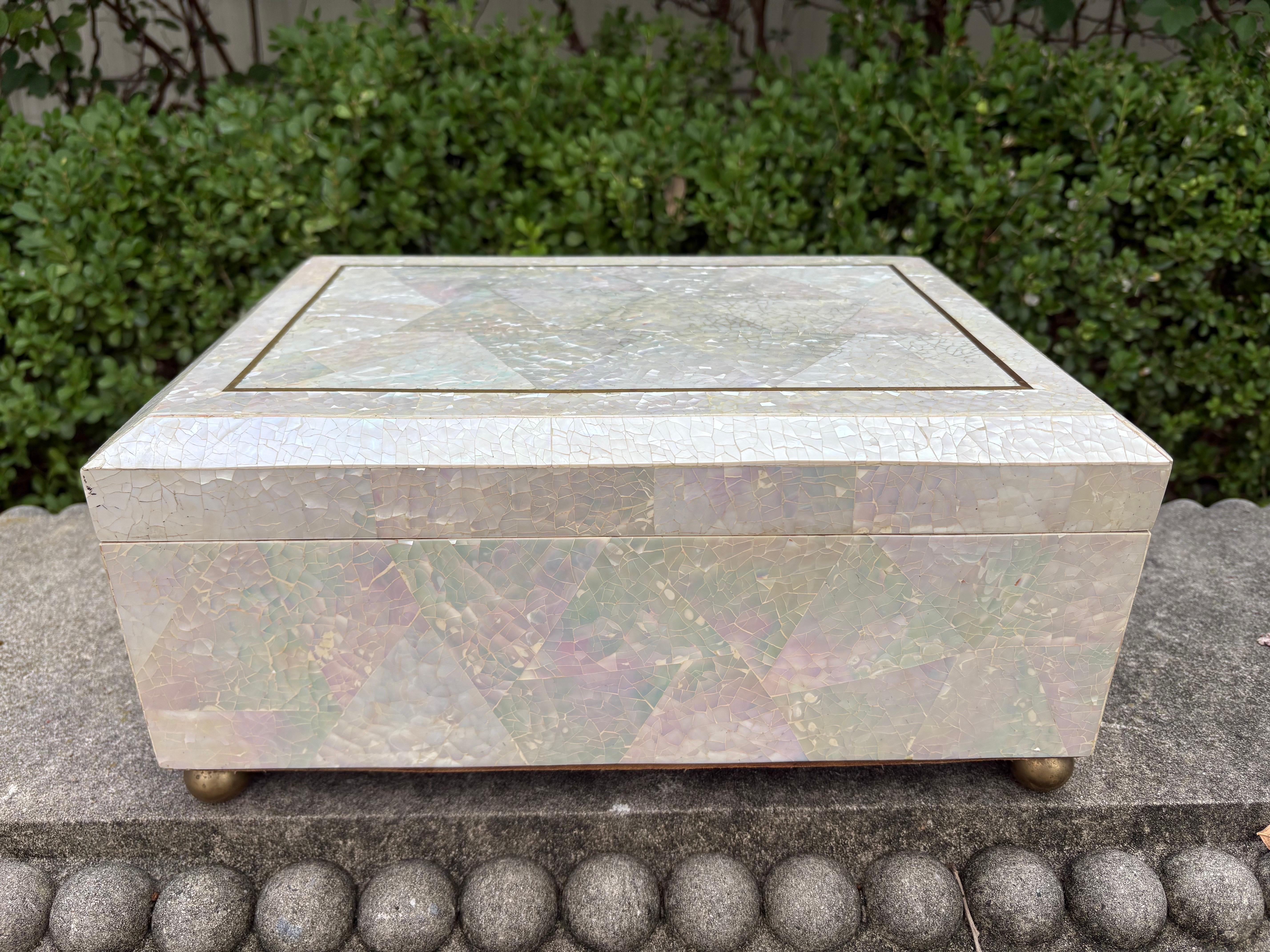 Maitland Smith Mother Of Pearl Box.
Offered is a very large decorative box of tessellated mother of pearl in the geometric Art Deco style with brass inlay and feet created by Maitland Smith. This handsome box is the perfect cocktail table or