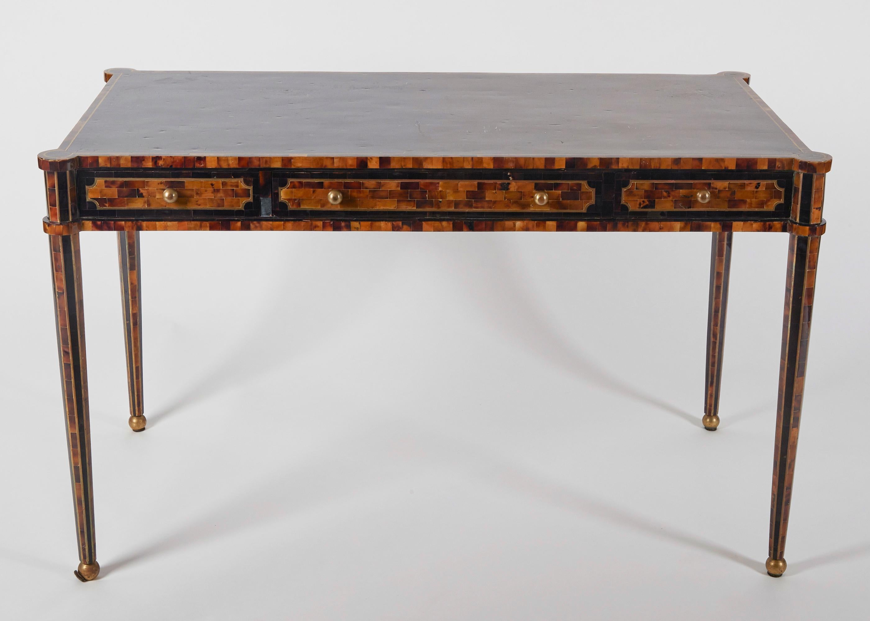 A Maitland-Smith veneered Neoclassical-inspired writing table. Possesses three drawers with brass pulls. Bearing original plaque.