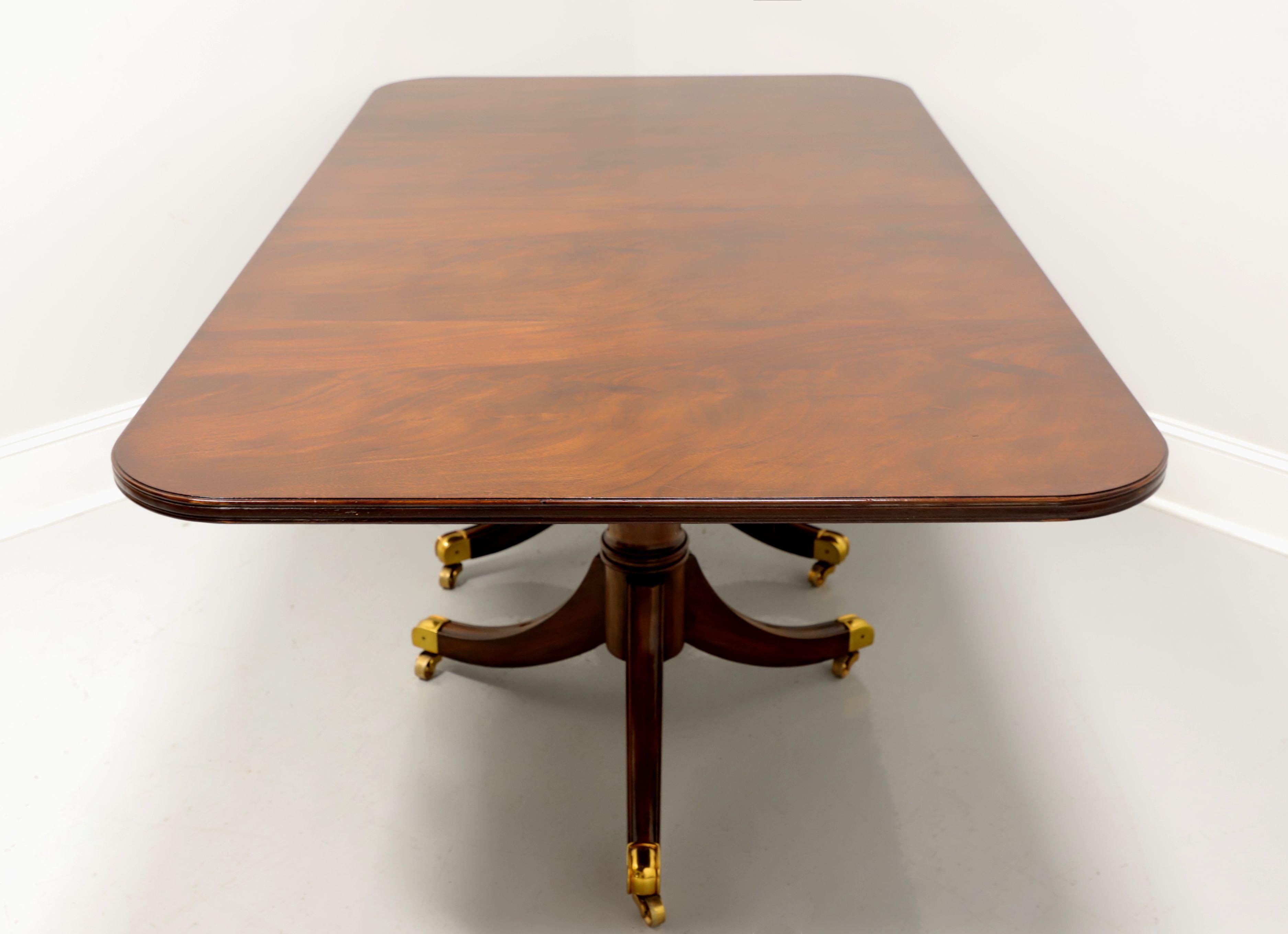 A Regency style rectangular dining table by Maitland Smith. Flame mahogany top, rounded corners, ribbed edge, mahogany double pedestal base with brass toe caps and casters. Metal expansion sliders. Includes two extension leaves. Hand made in the
