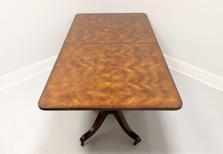 A Regency style rectangular dining table by Maitland Smith. Flame mahogany top, rounded corners, ribbed edge, mahogany double pedestal base, four legs with brass toe caps and casters. Includes one extension leaf for placement on expansion sliders.