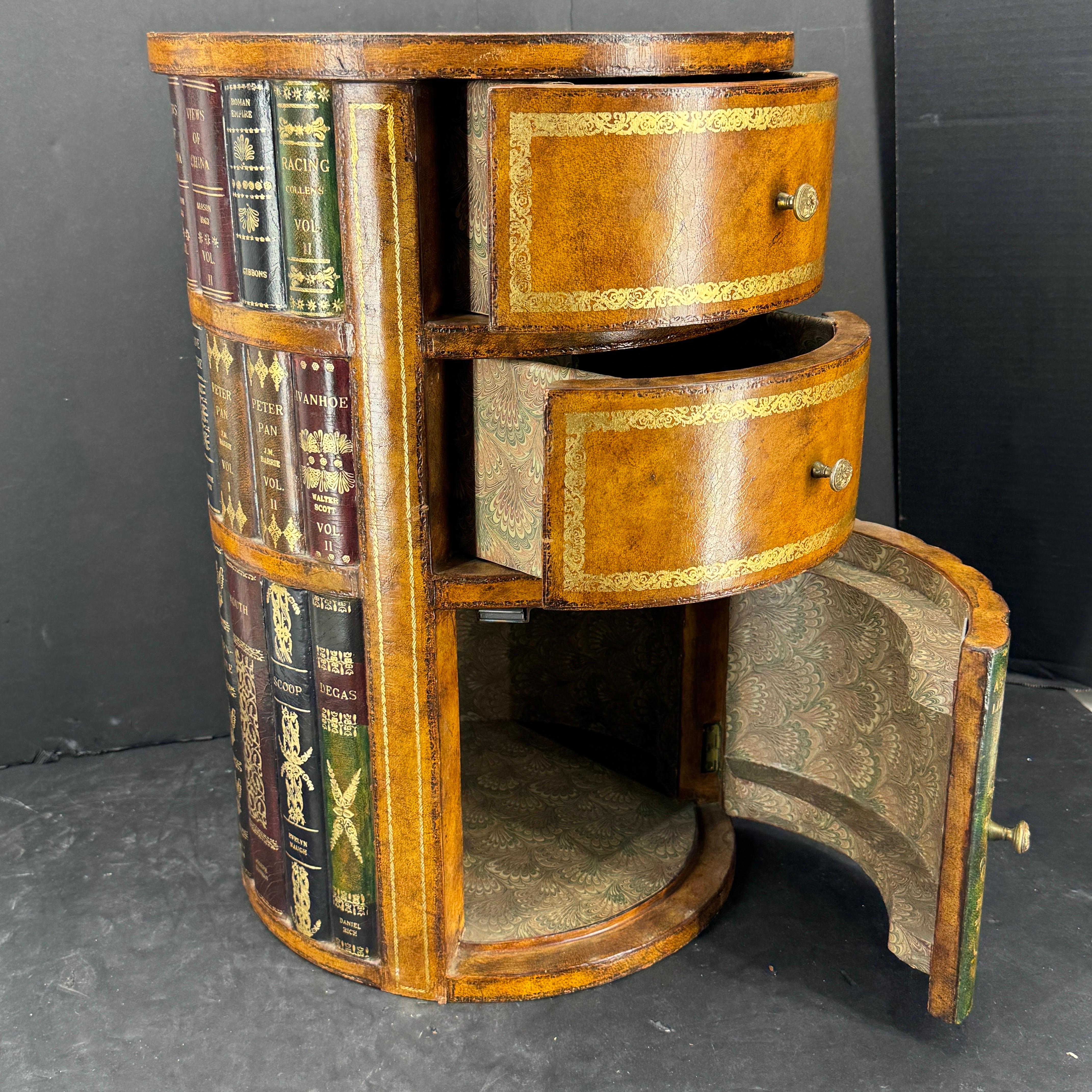 Charming Chesterfield-like round gilt tooled leather-bound end or side table by Maitland Smith. There are gilt edges throughout with two drawers as well as storage at the bottom featuring faux library books. Great statement piece in a living room as