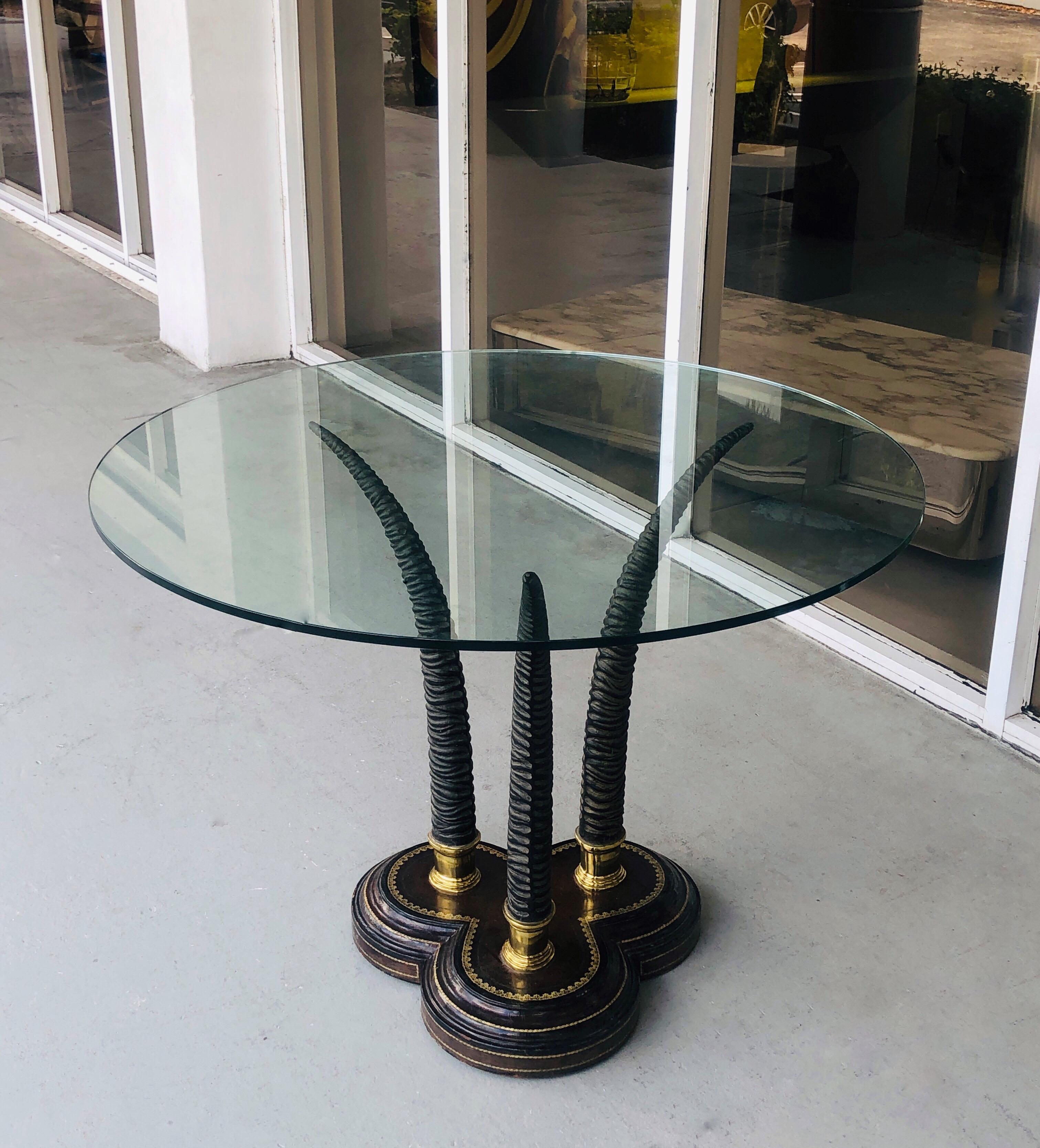 A round table by Maitland Smith. The base is leather bound, with 3 metal horns mounted on brass. Original glass top is 40” in diameter.