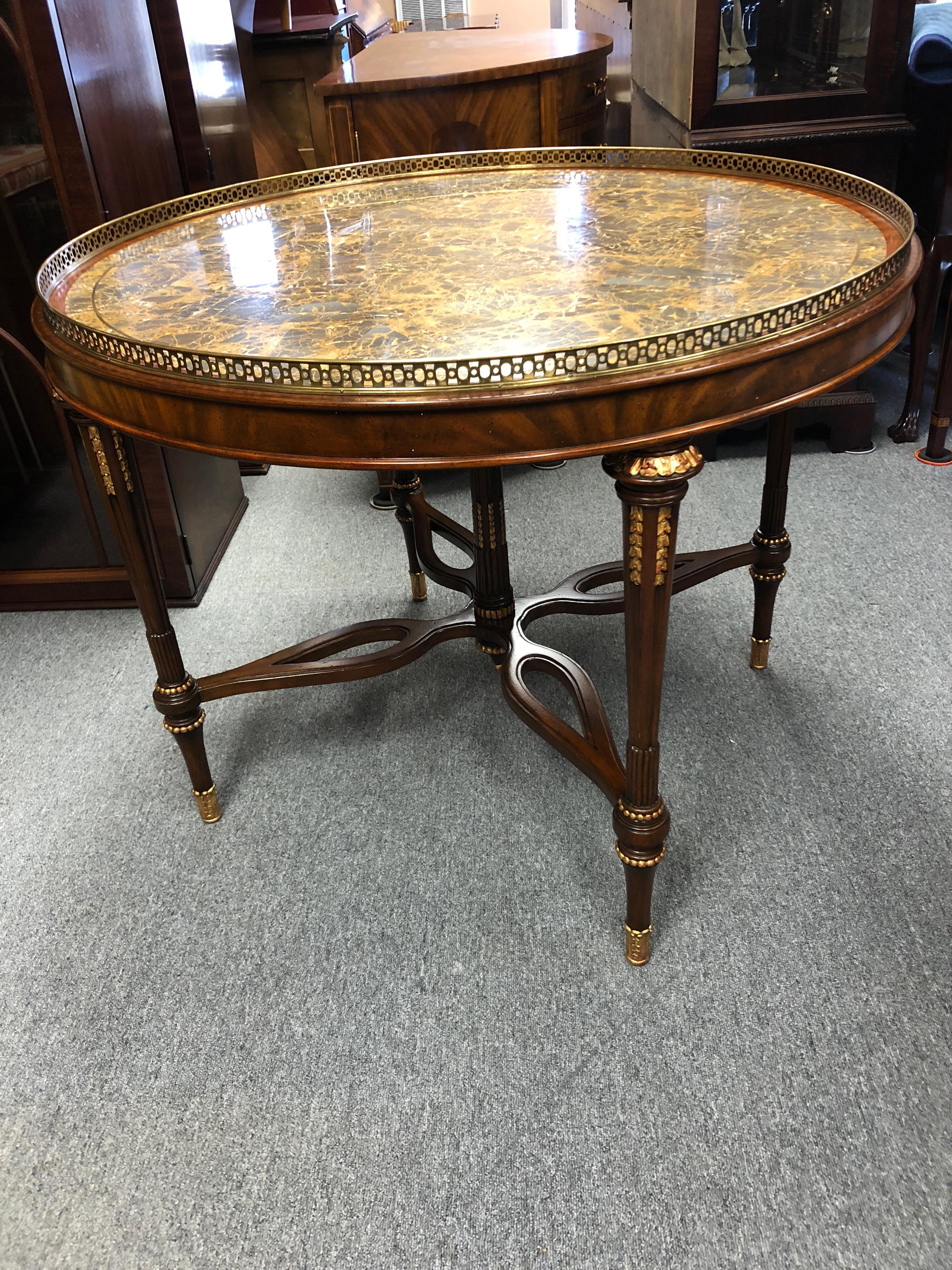 Impressive round center or side table by Maitland Smith having an inlaid faux marble top with pierced brass gallery and decorative brass band, with a gorgeous mahogany and gilded ornate base with particularly pretty central column and stretcher