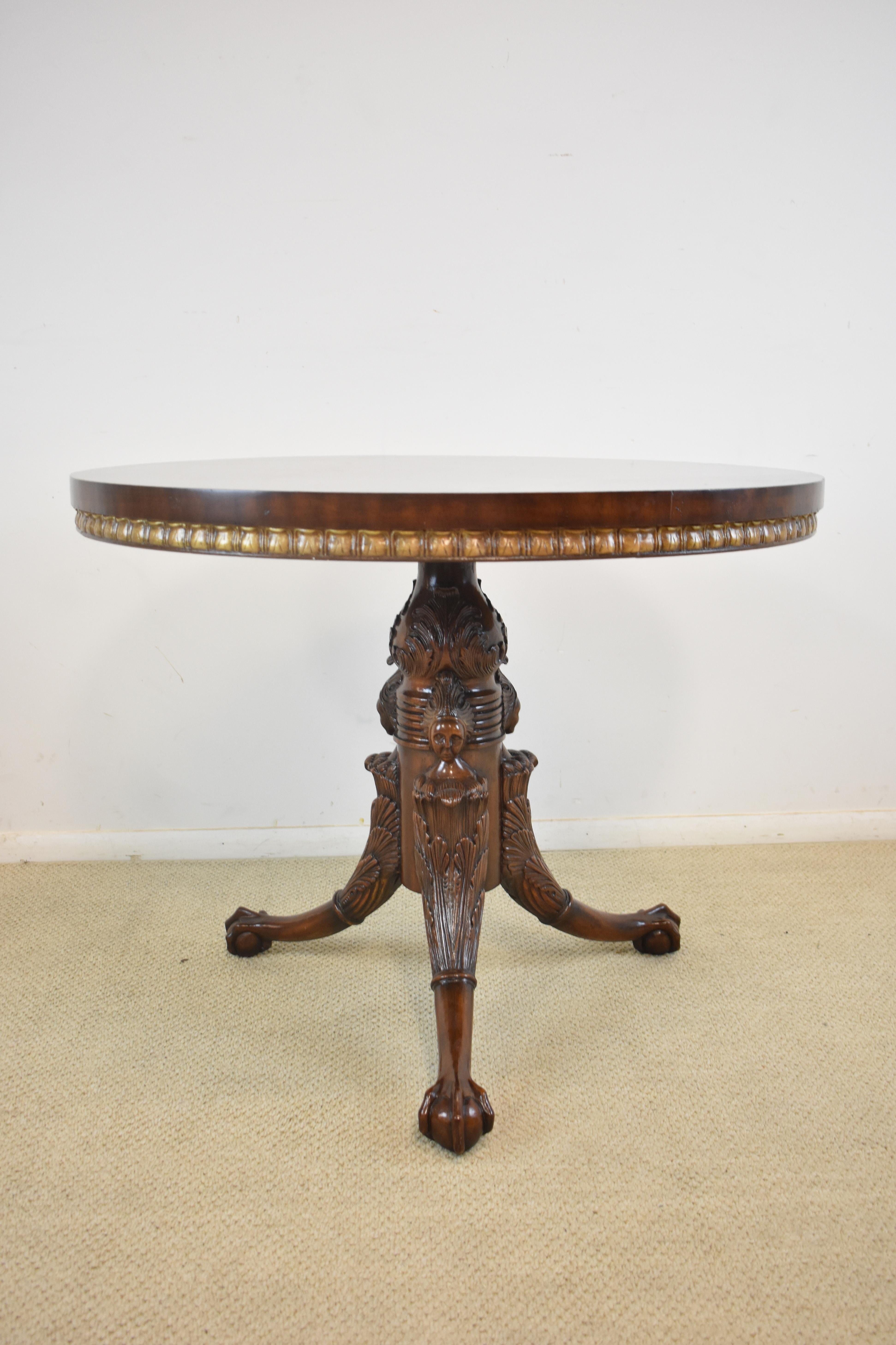 An elegant round centre table by Maitland Smith. Mahogany with a hand-carved tripod base that features female figures and ball and claw feet. The round burled top has a gold gilt banding around the edge. This table is in beautiful condition.
