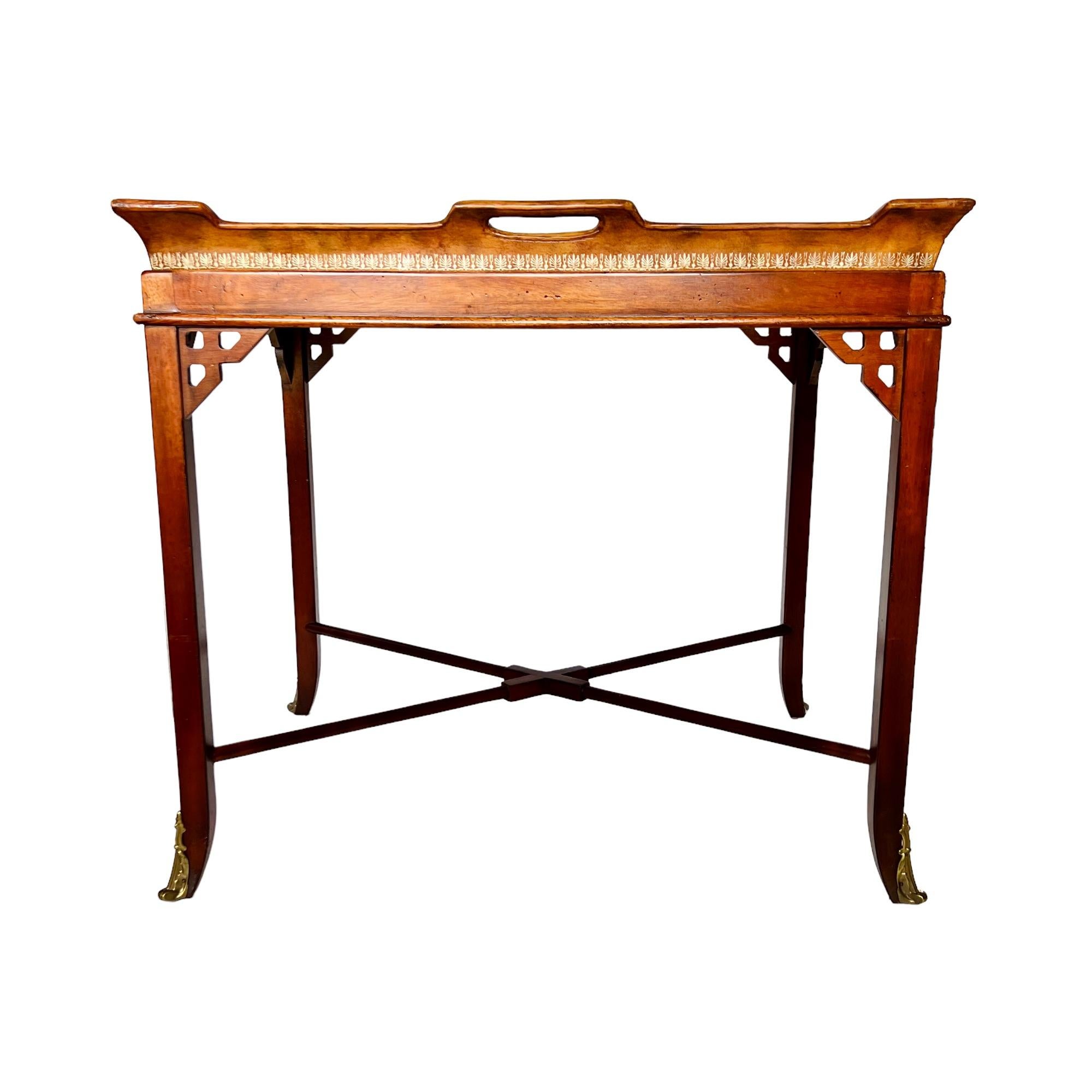 A late 20th century regency style mahogany, embossed leather & glass tray top accent table attributed to Maitland Smith. Wood frame with pierced corner details, brass mounted tapered feet and x-form stretcher base. Leather-wrapped tray top features