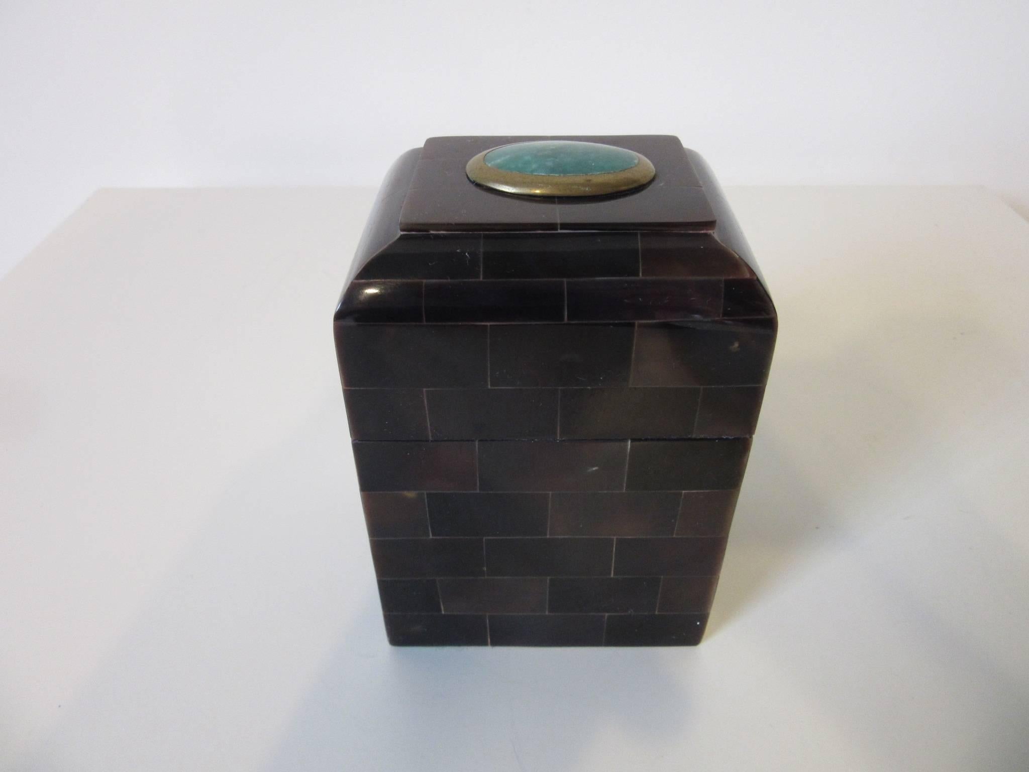 A decorative box with tessellated horn in dark brown tones and a blue green gem stone to the lid surrounded by a brass bezel. When opened the inside revels a caramel colored Philippine mahogany interior, retains the manufactures label to the bottom