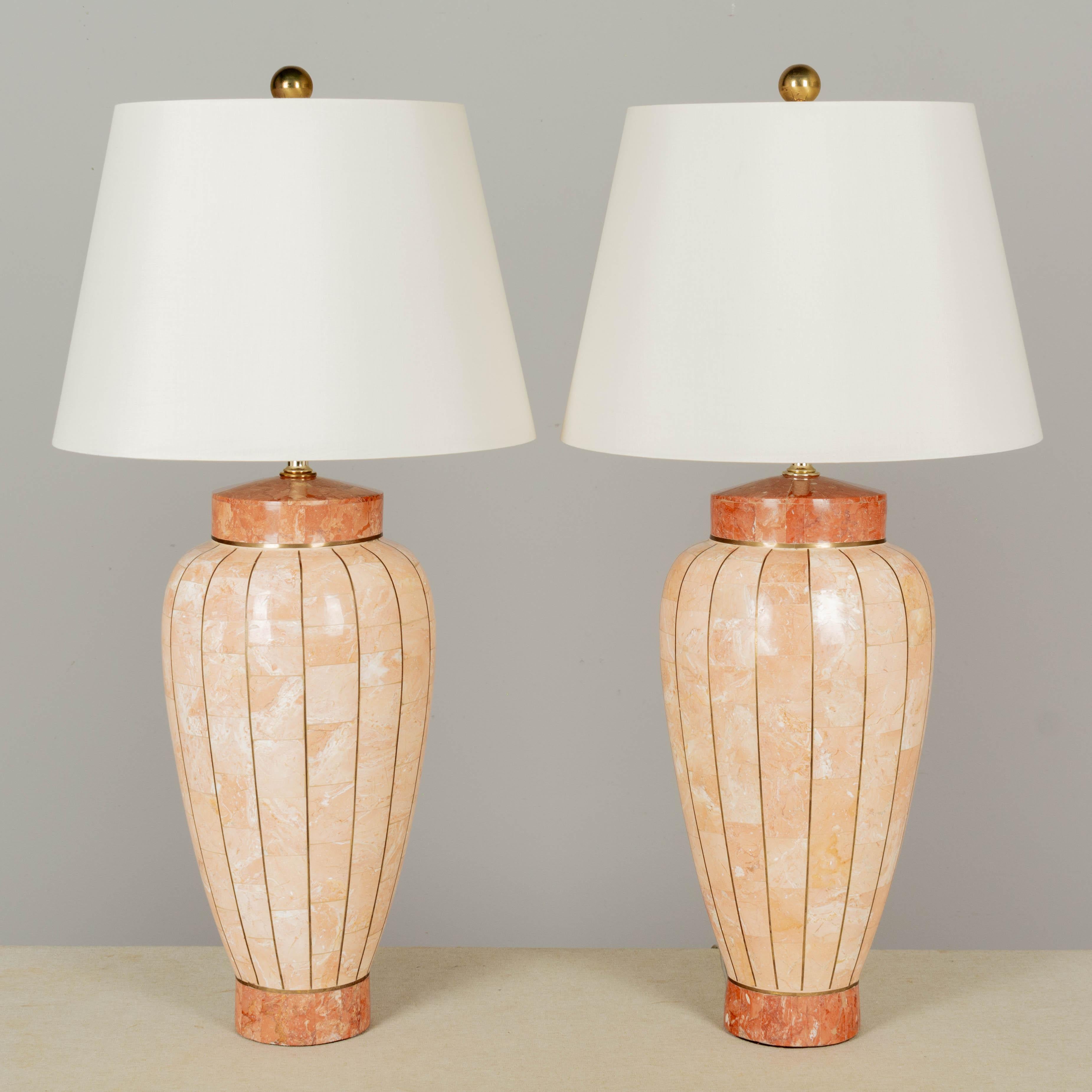A pair of Maitland Smith tessellated stone table lamps with thin strips of brass inlay. Beautiful seashell peach polished marble tile body with coral color at the base and top. Large brass ball finials. Rewired with new sockets and cords. Excellent