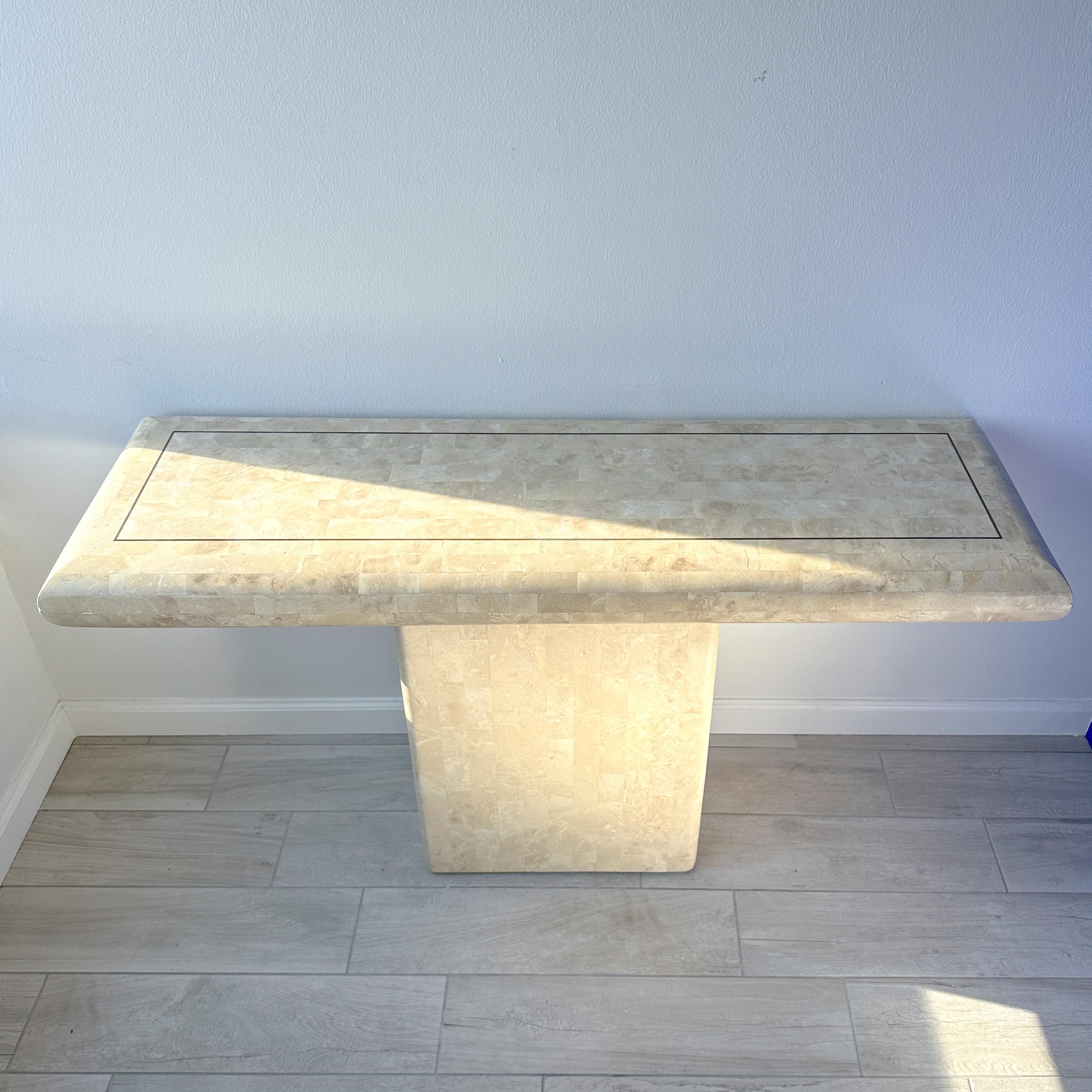 Circa 1970s Maitland Smith tessellated travertine stone console table with brass inlay. Pedestal table with bullnose rounded edges and brass inlay rectangle on top.
