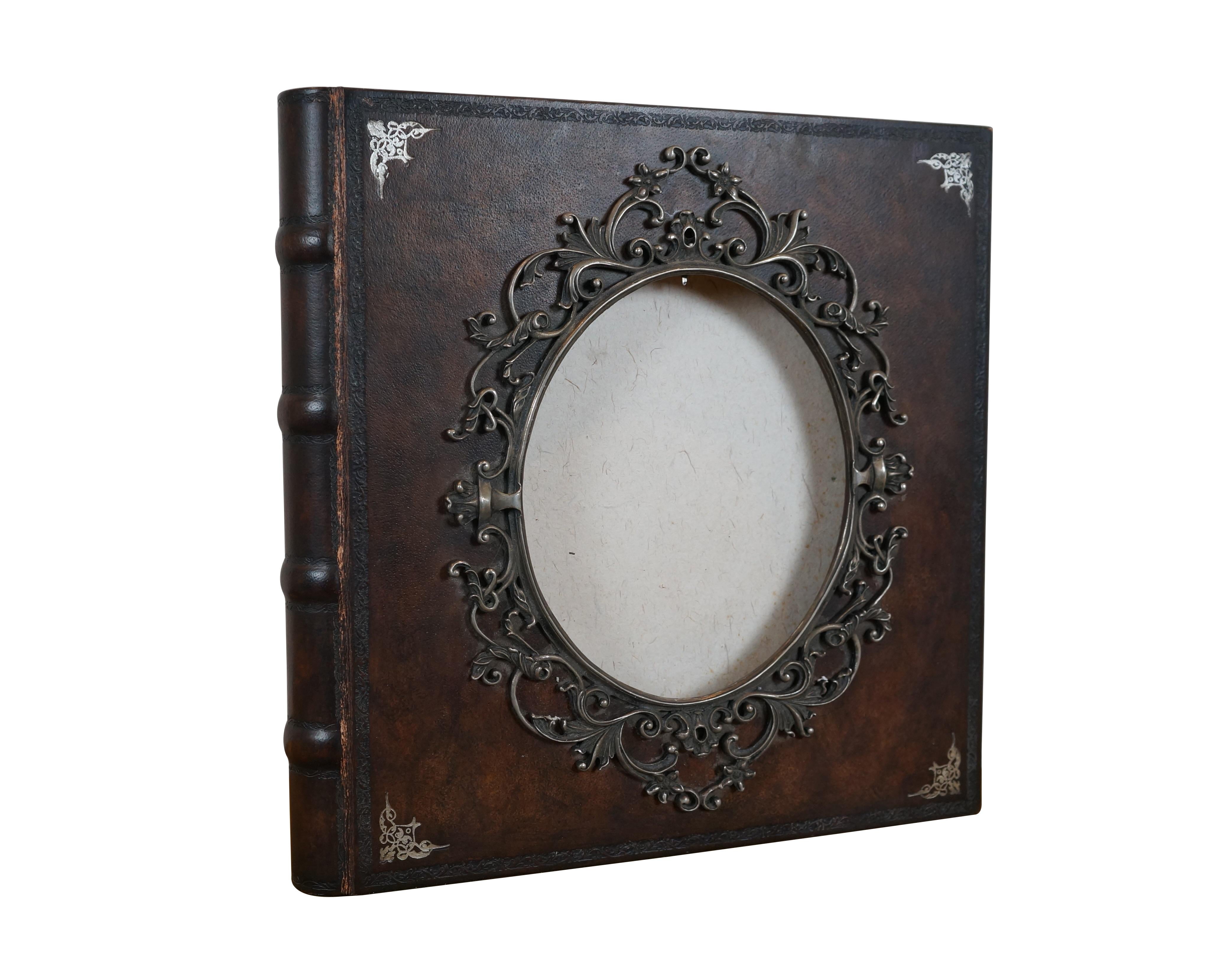 Late 20th century Maitland Smith tooled leather memories photo album scrap book with wooden spine and stamped gilt details. Front of cover incorporates an oval photo space with an ornate silverplate foliate picture frame. Contains approximately 75