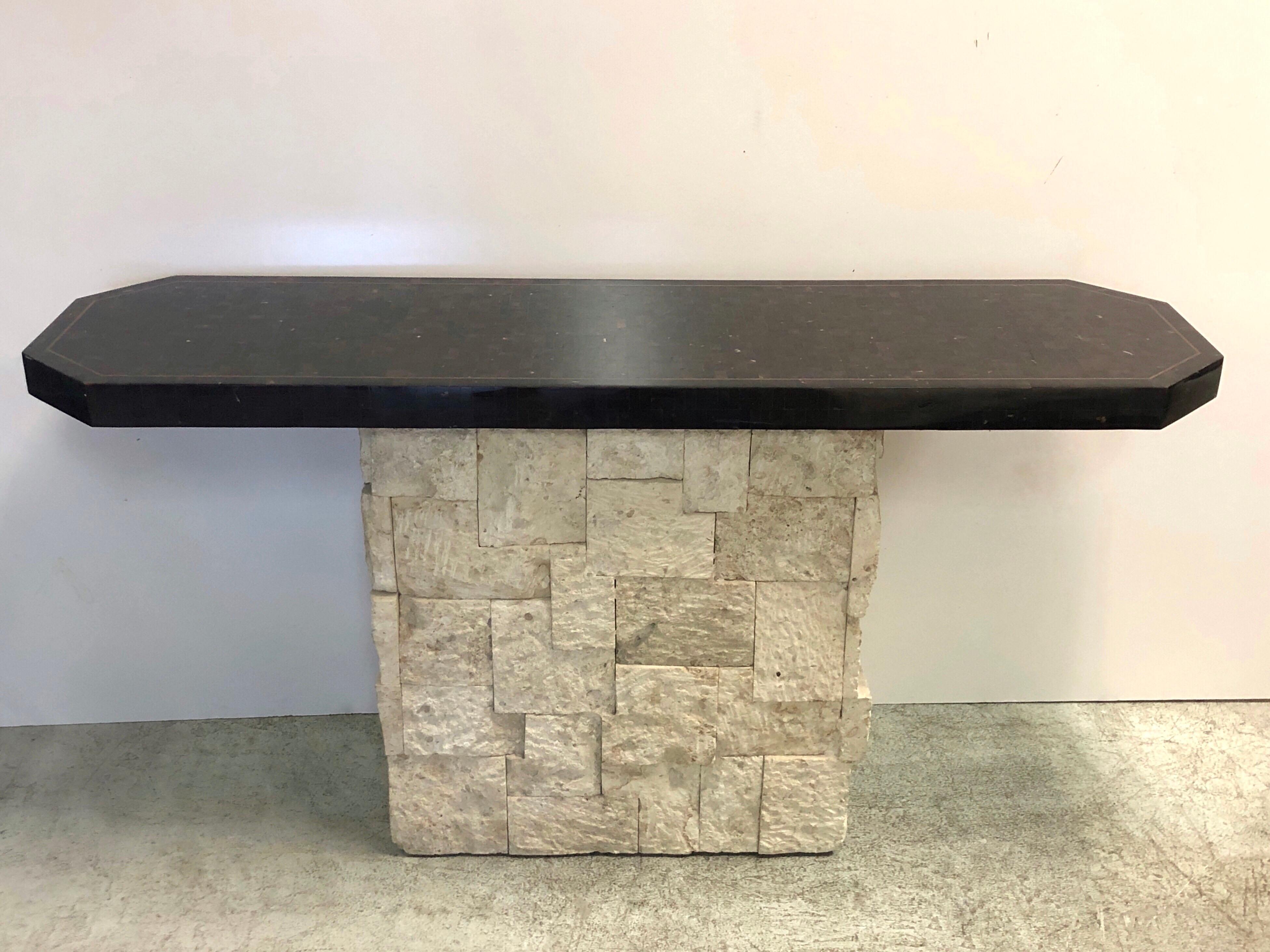 A console table by Maitland Smith. The rectangular base is made of multiple pieces of raw travertine in different sizes and depths. The top is tessellated faux tortoise with brass inlaid. Finished on all sides.
