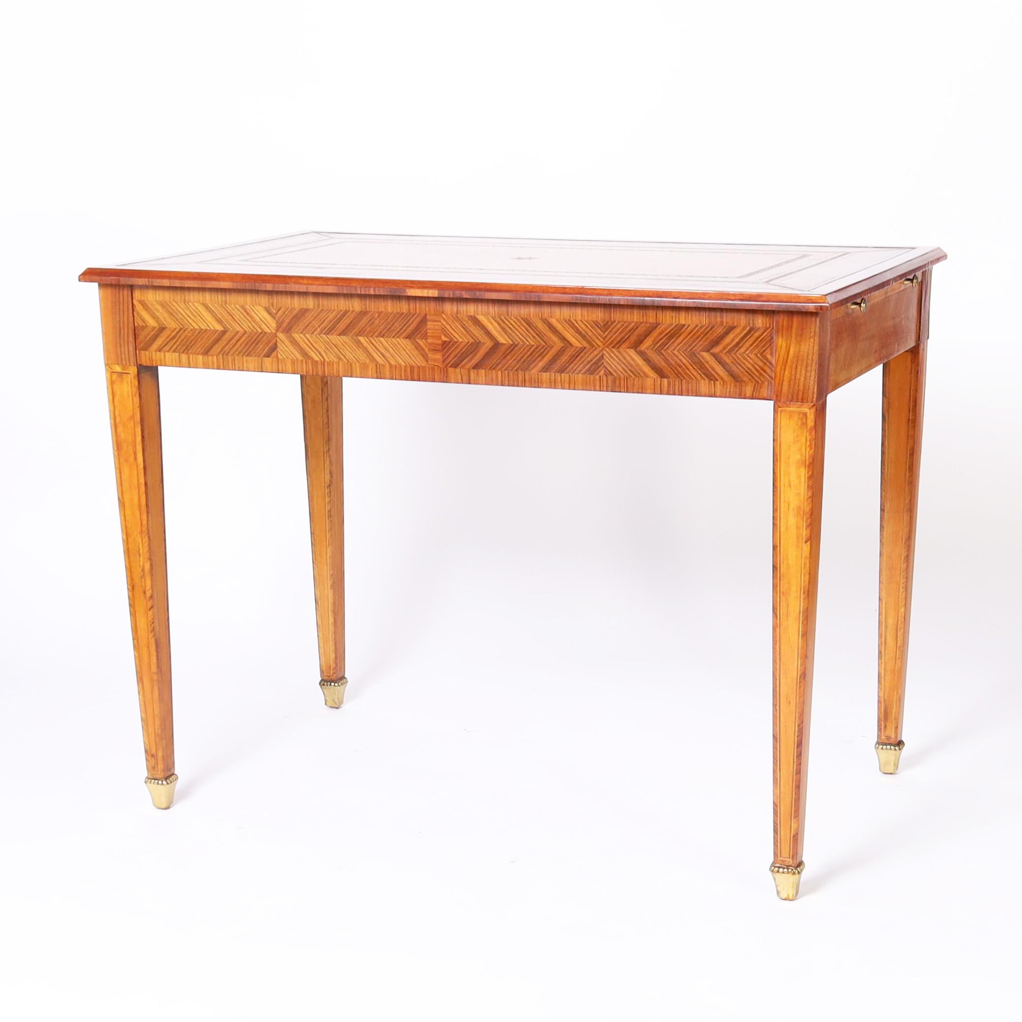 Impressive mid century writing desk with a pleasant mixture of French and English influences featuring a tooled leather top on a rosewood case having two drawers and two pull out trays with brass hardware. The elegant tapered legs have inlaid