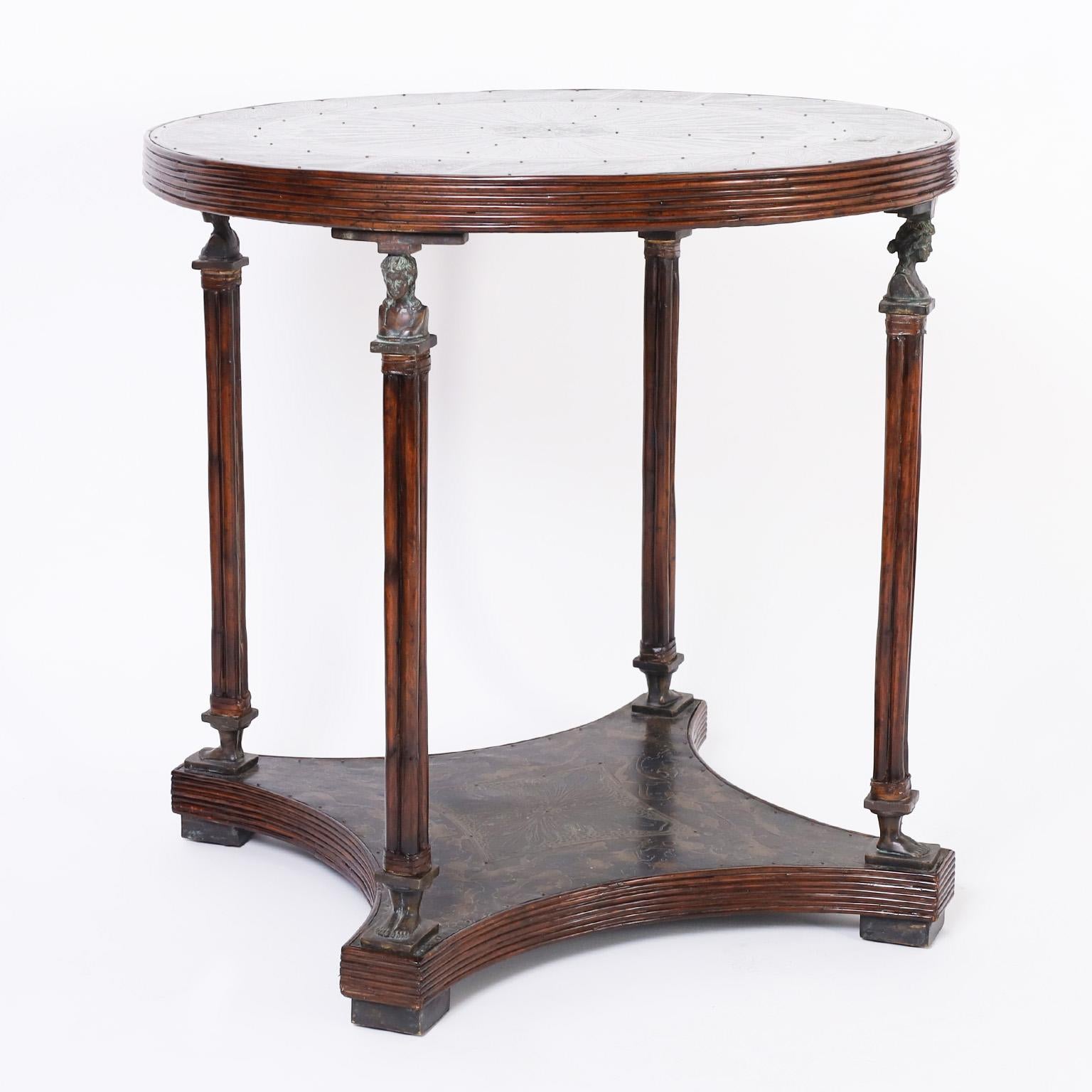 Midcentury table or stand handcrafted in an unusual mix of materials having a bronze top and lower tier with etched floral designs and multiple patinas in a pencil reed frame over mahogany supports with classical bronze busts, legs and block feet.