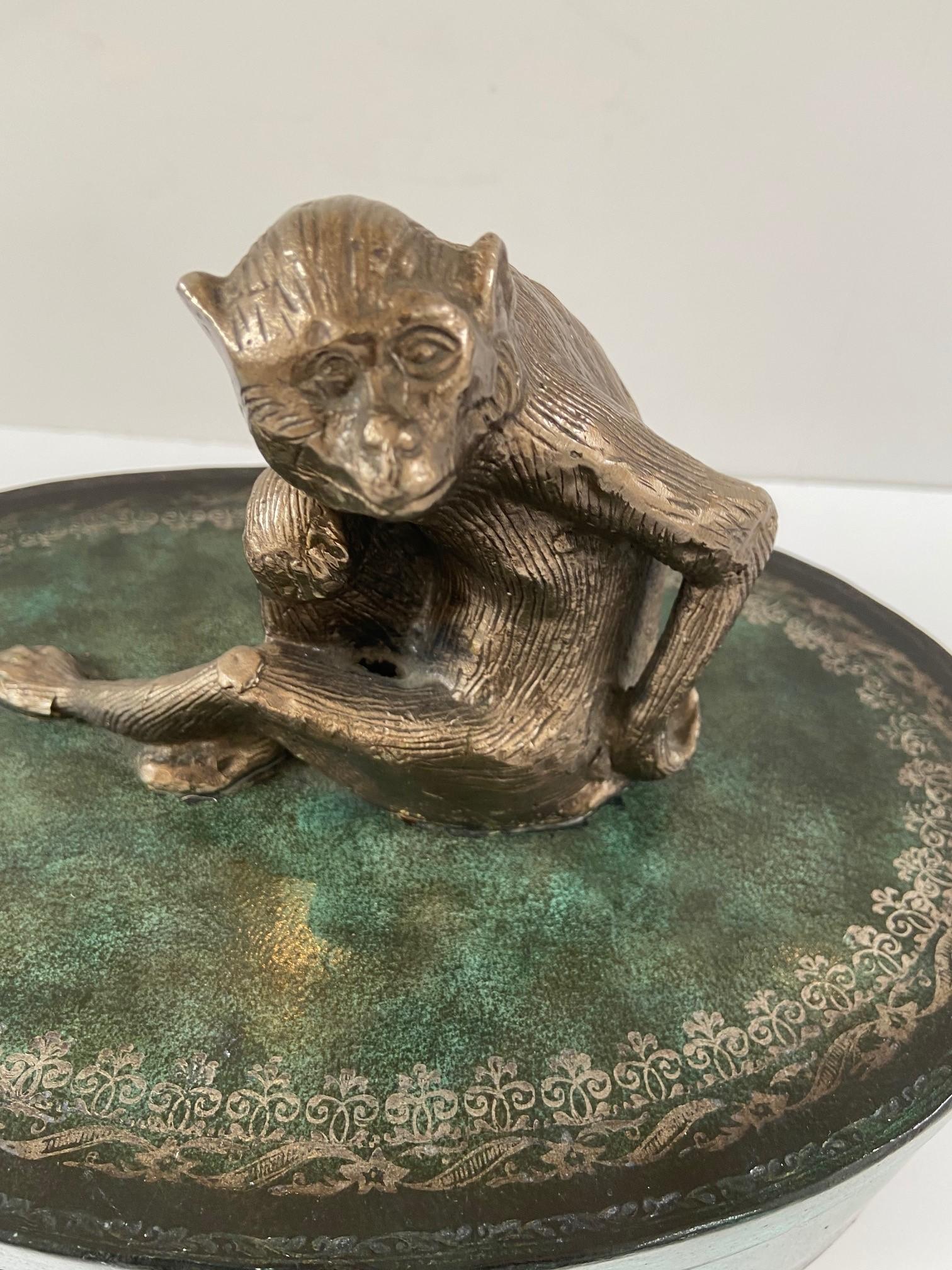 Maitland Smith with cast figural metal monkey on a wood box, features the form of a monkey crafted in cast metal and silver in tone, wood base with faux green leather decoration embellished with an embossed silver tone pattern.