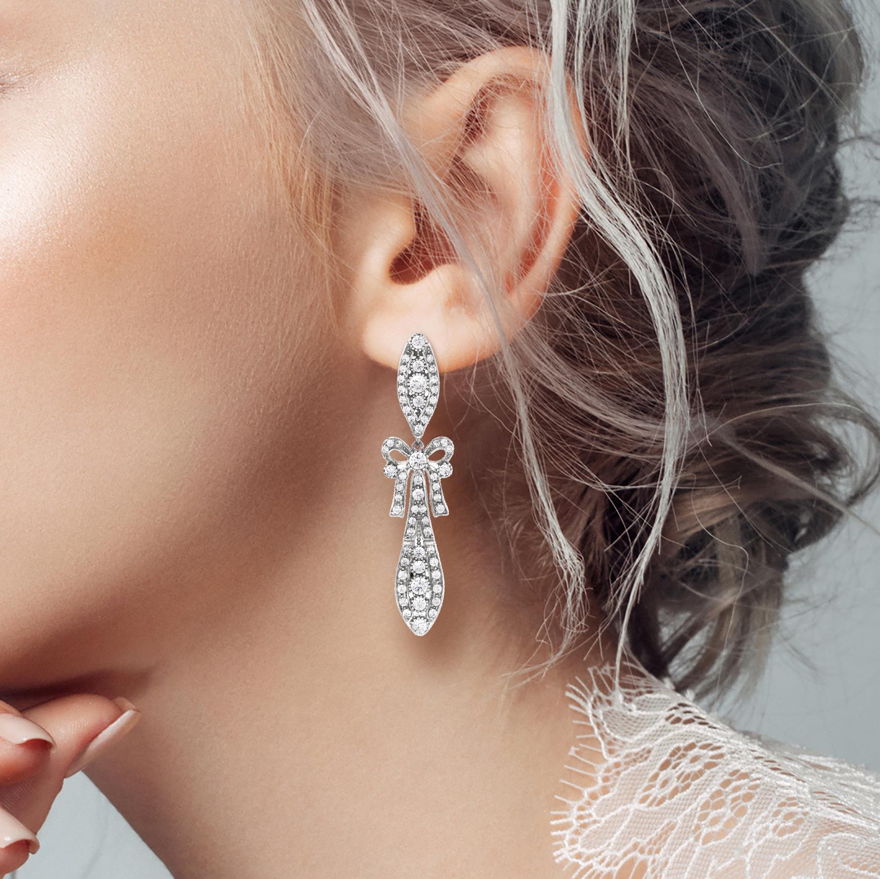 Stunning Art Deco style dangle earrings in 18k white gold featuring 60 sparkling diamonds worked info a feminine bow and foliage design.

Information
Metal: 18K White Gold
Width: 12 mm.
Length: 52 mm.
Weight: 15.07 g. (approx. total weight)
Backing: