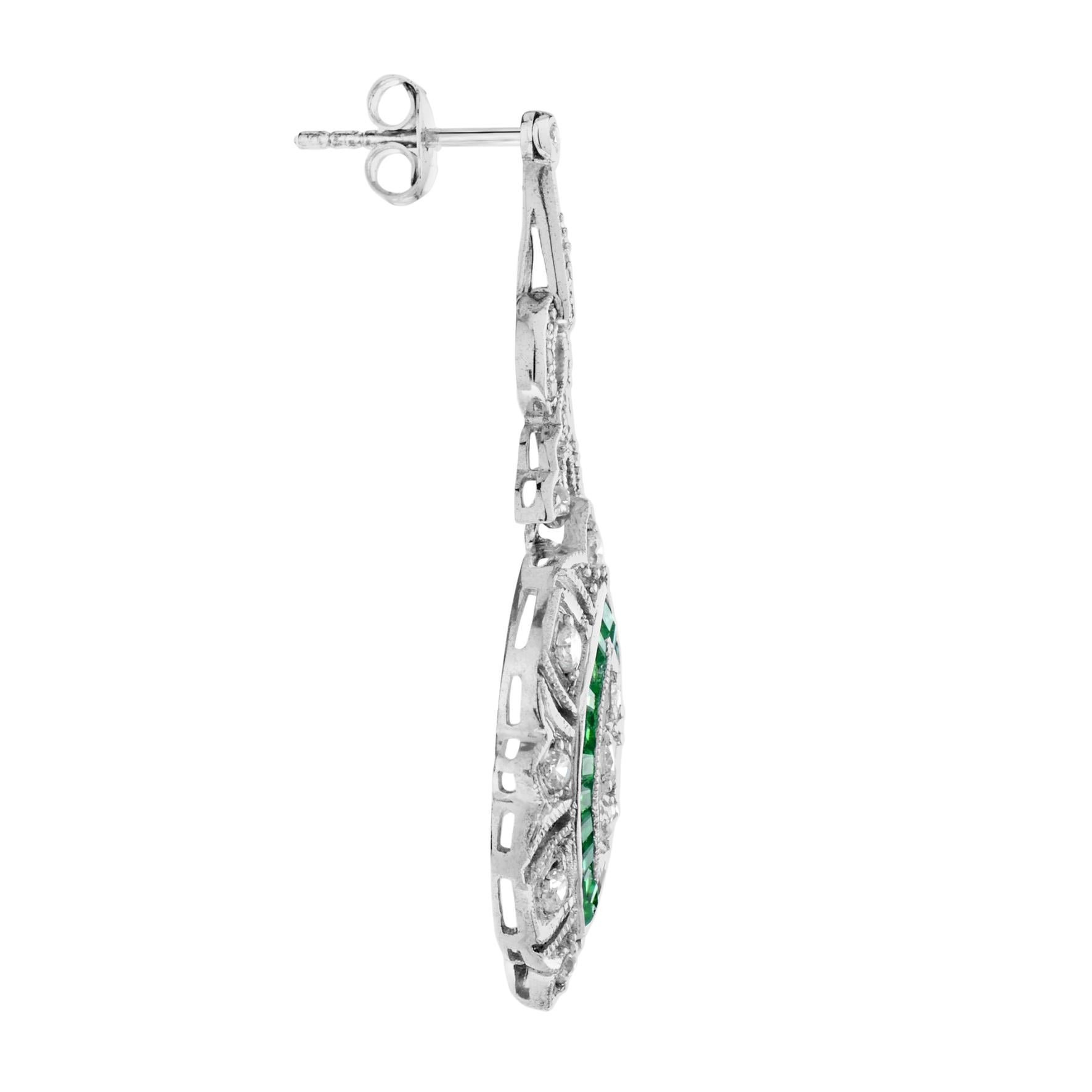 These beautiful Art Deco-style dangle earrings are finished in brightly polished 18K white gold. Delicately set across the face of the earrings are three round diamonds surrounded by French-cut natural emeralds. The entire earring is adorned with
