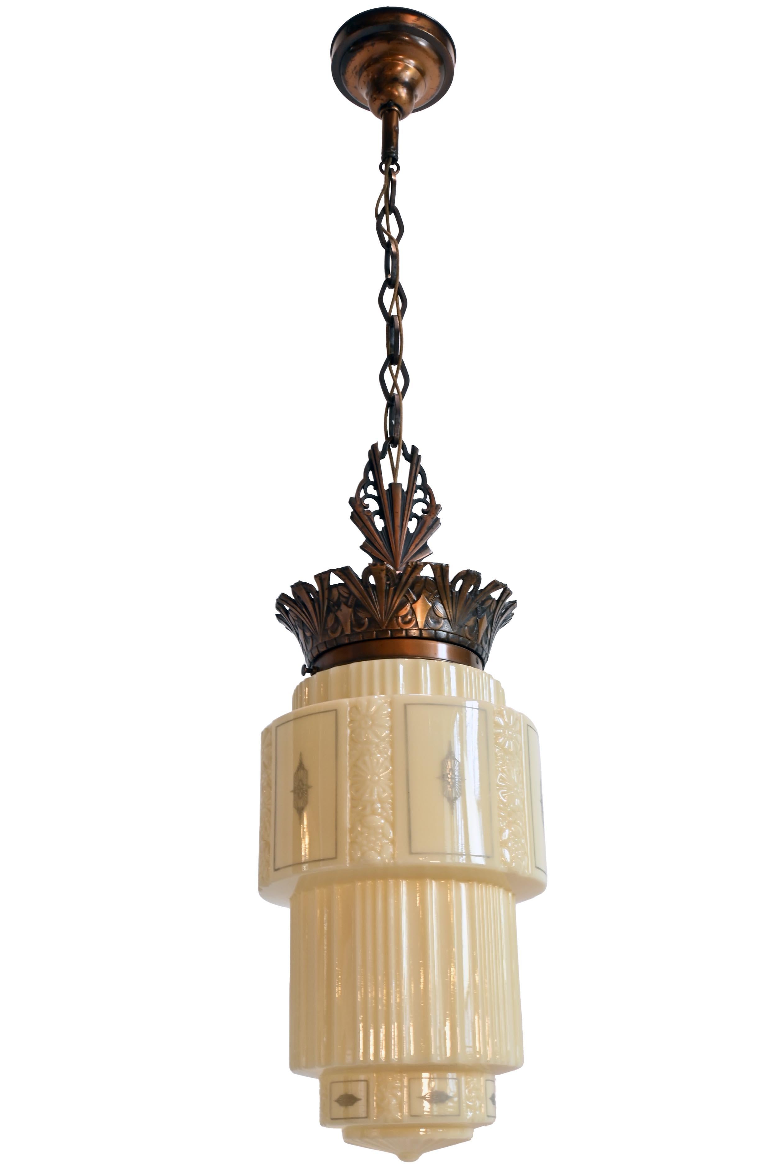 This finely crafted pendant features an Art Deco design and intricate stenciled details on a rarely seen custard glass shade. A pleasing mix of sharp lines and soft curved crown adorn the Bronze Plated frame. This pendant has a skyscraper design