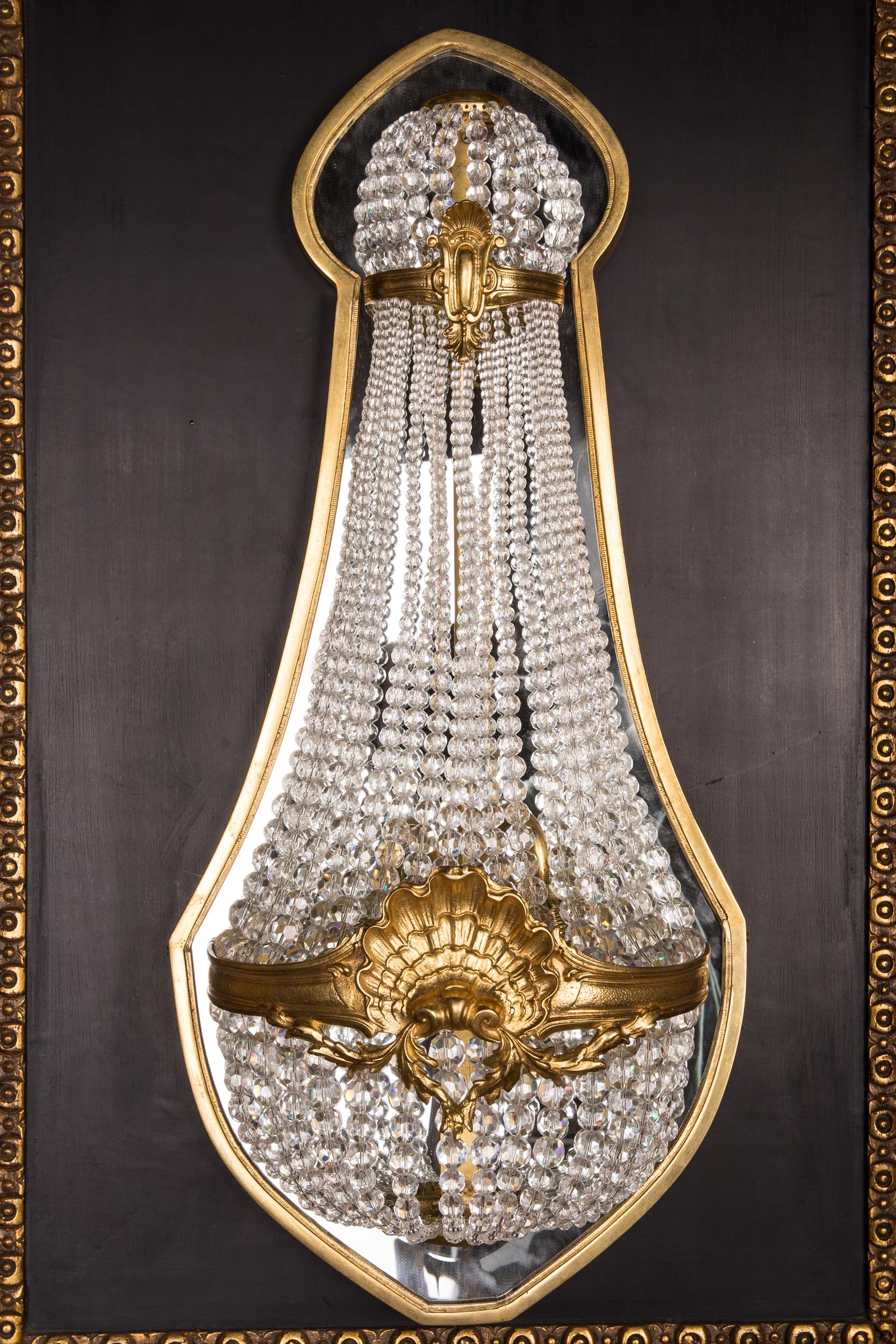 A classicist sconce with finely engraved bronze. Basket-shaped body made of handcut franz. Sphere prisms in the course connected by broad, ornamental relief-shaped hoop in the center of the attached shell. The finely polished crystals break and