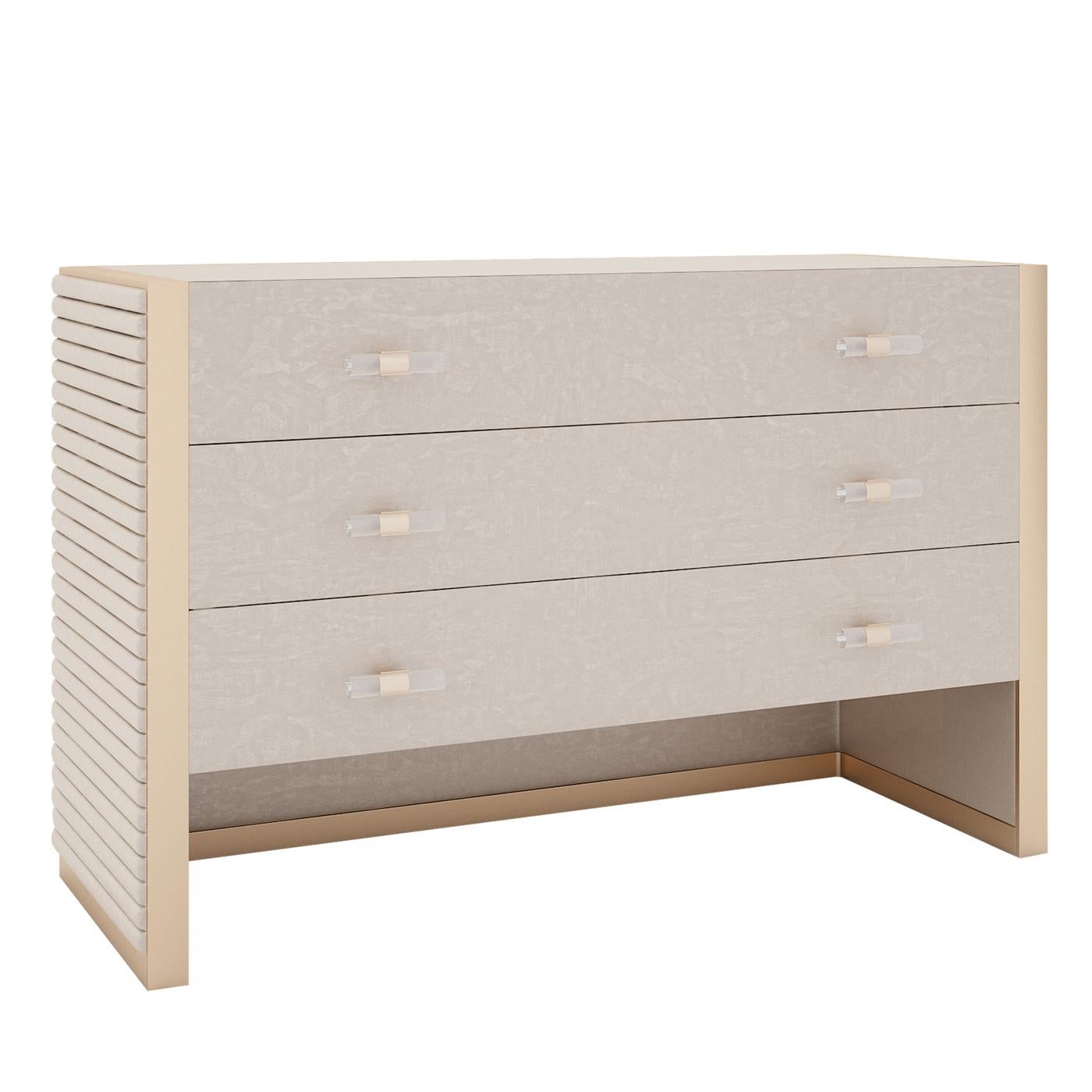 Showcasing a superbly refined and solid silhouette, this dresser is aptly named Majestic. Brass-finished metal inserts outline its main lines, including the three drawers' handles, and splendidly complement the upholstery in light gray fabric