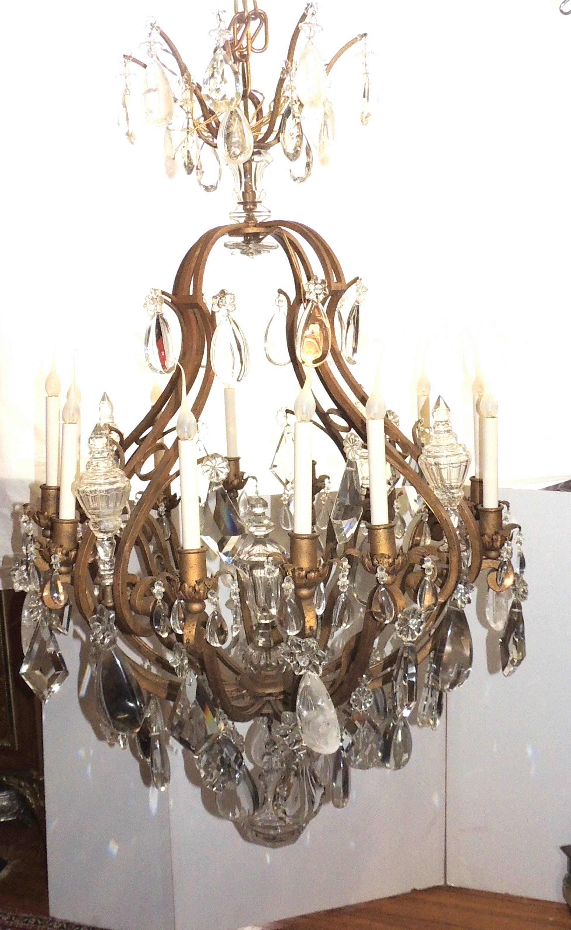 This wonderful very large 1920s gilt iron French cage chandelier has twelve lights with an assortment of flat, prism, faceted and rock crystals finished with a large beveled ball at the bottom. In the Baguès manner

Measures: 55