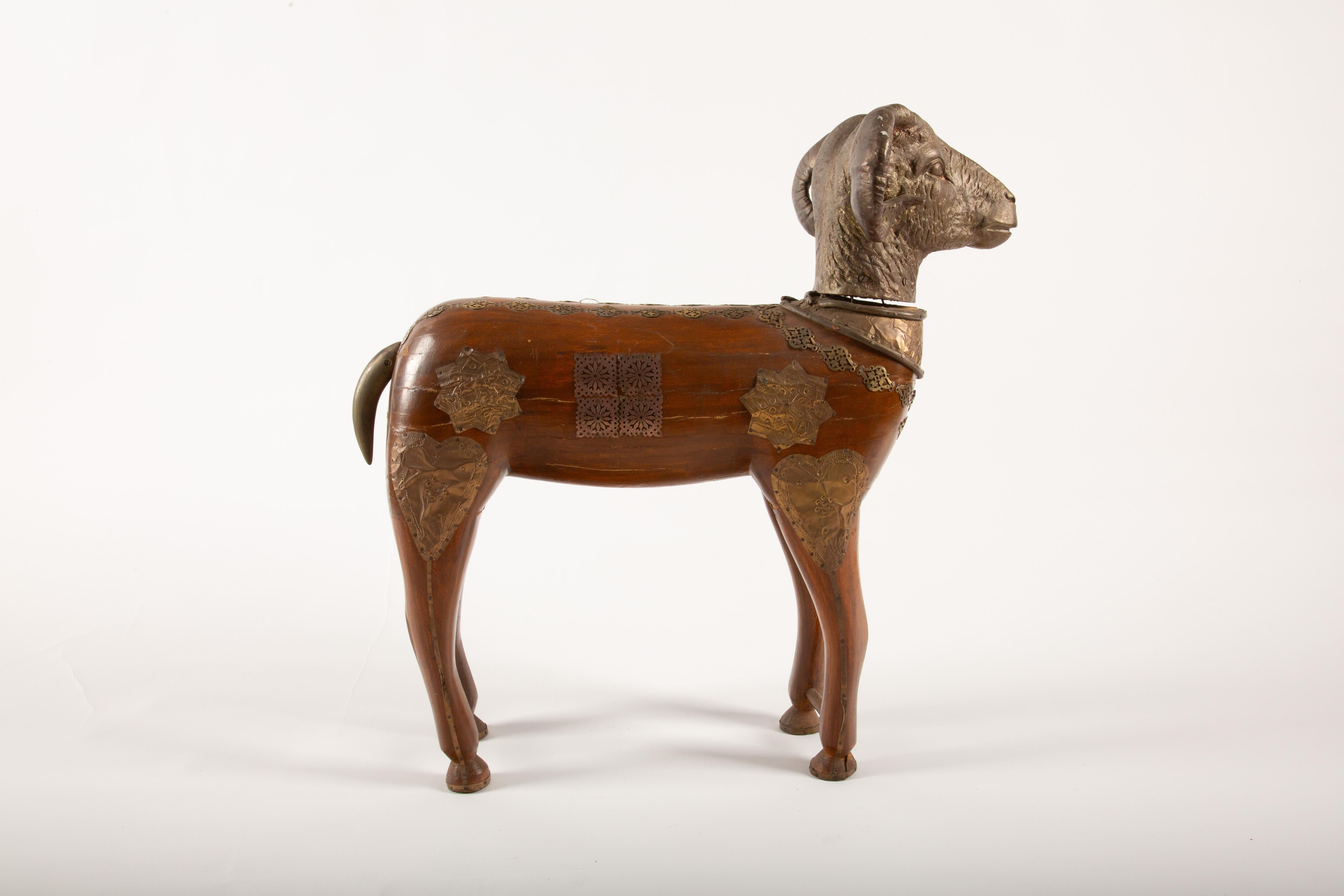 This large Indian brass-mounted wooden ram figure is a remarkable example of traditional craftsmanship, blending the natural beauty of wood with intricate brass appliqués. The carved wooden body is adorned with detailed brass decorations, including