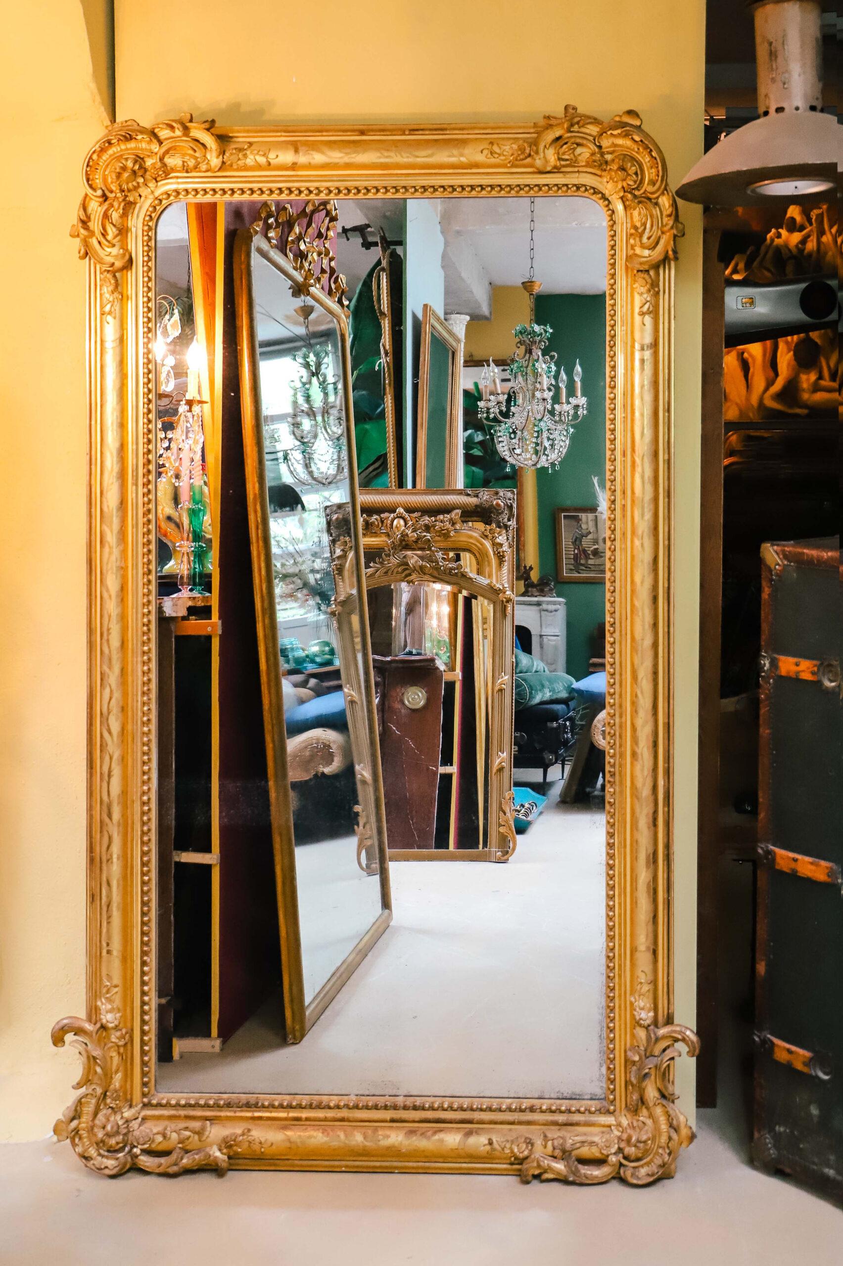 Plongez dans la grandeur de ce superbe miroir ancien français du 19e siècle de style Louis Philippe, doré à l'or fin. Le cadre épais est orné de feuilles et de fleurs complexes dans les coins supérieurs et inférieurs, accentuées par des perles le