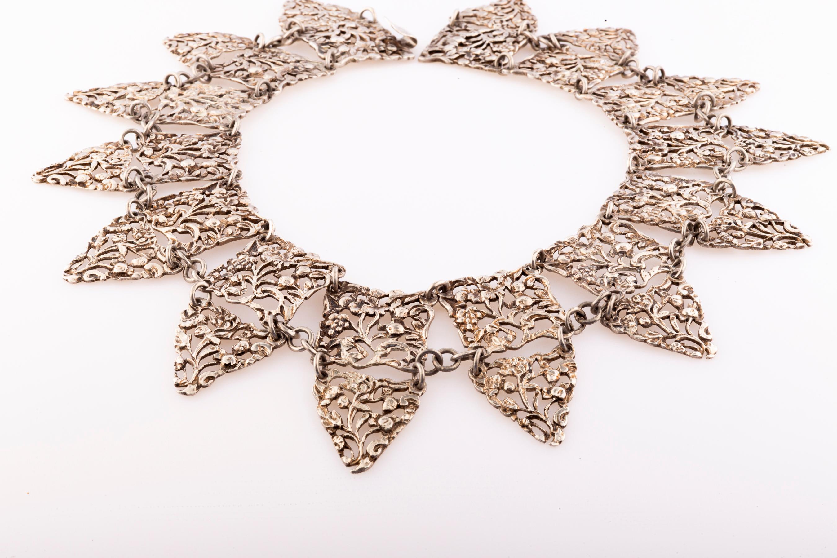 Suntuosas en Sterling, catorce placas cuadradas están grabadas abiertamente con bayas, flores y hojas que muestran la apreciación Art Nouveau del mundo natural. Esto por sí solo sería precioso, pero los eslabones triangulares suspendidos hacen que