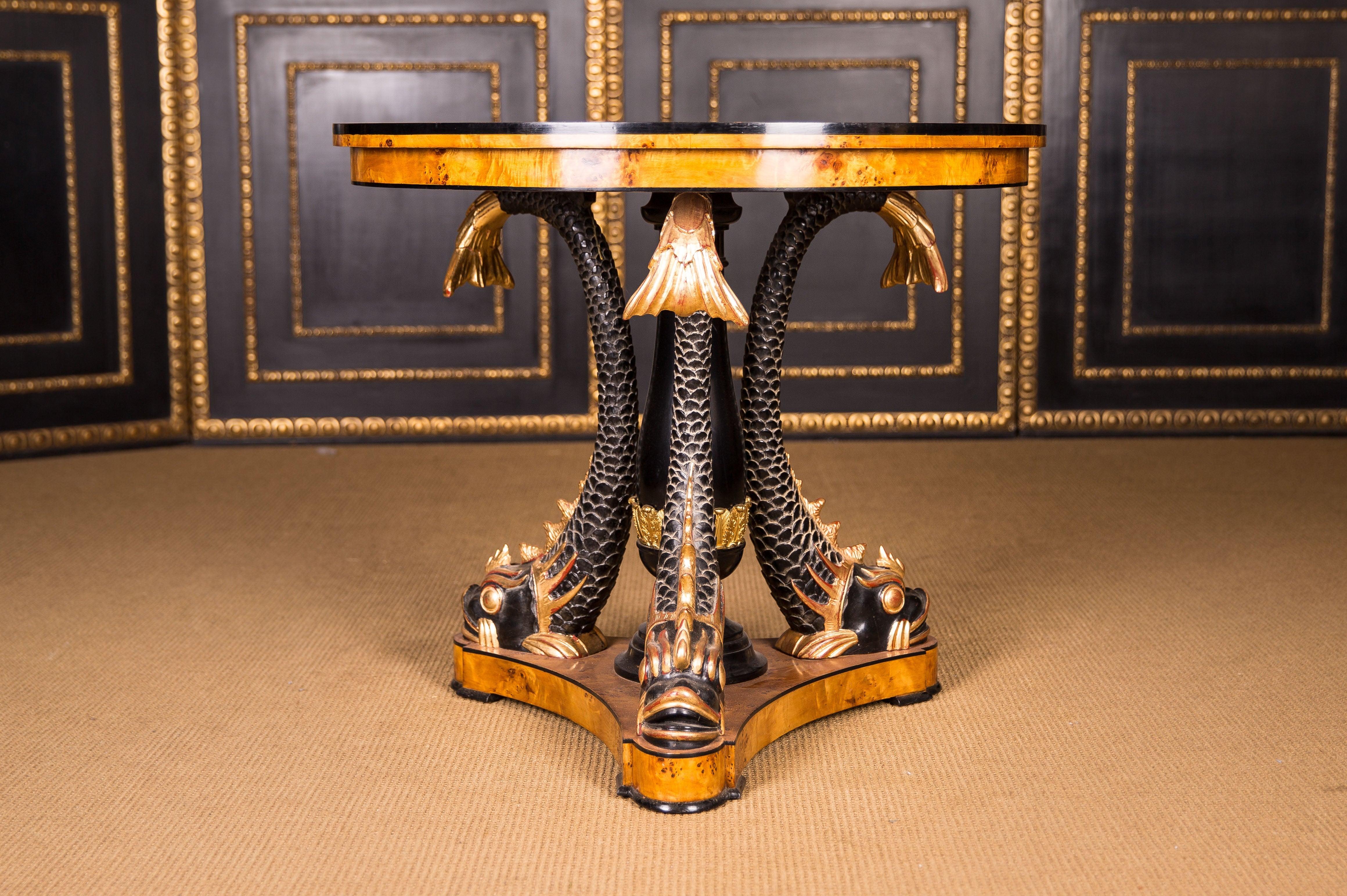 Maple root on solid beechwood. A classicist table with three monumental, full-plastic, hand carved dolphins made of solid wood. Shed colored, heads and fins are antique gold and framed in black. Three-sided base plate on glass panes. Centrally