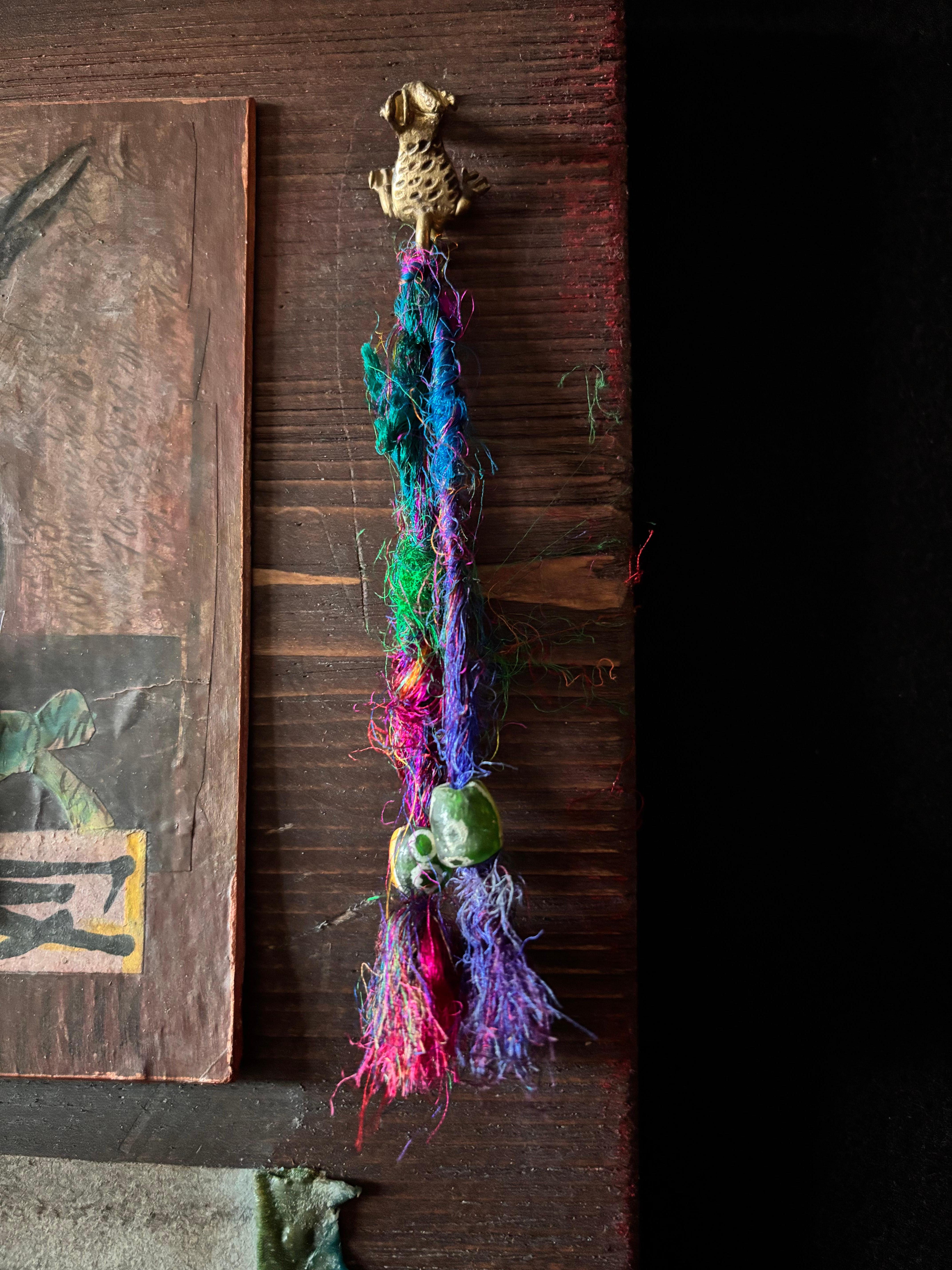 Présence d'une corneille noire et d'une grenouille. Un petit enfant plane au-dessus d'un oiseau noir qui prend son envol. En équilibre sur un côté, une autre grenouille... en guise de crochet en laiton. De l'autre côté, un objet rituel suggérant des