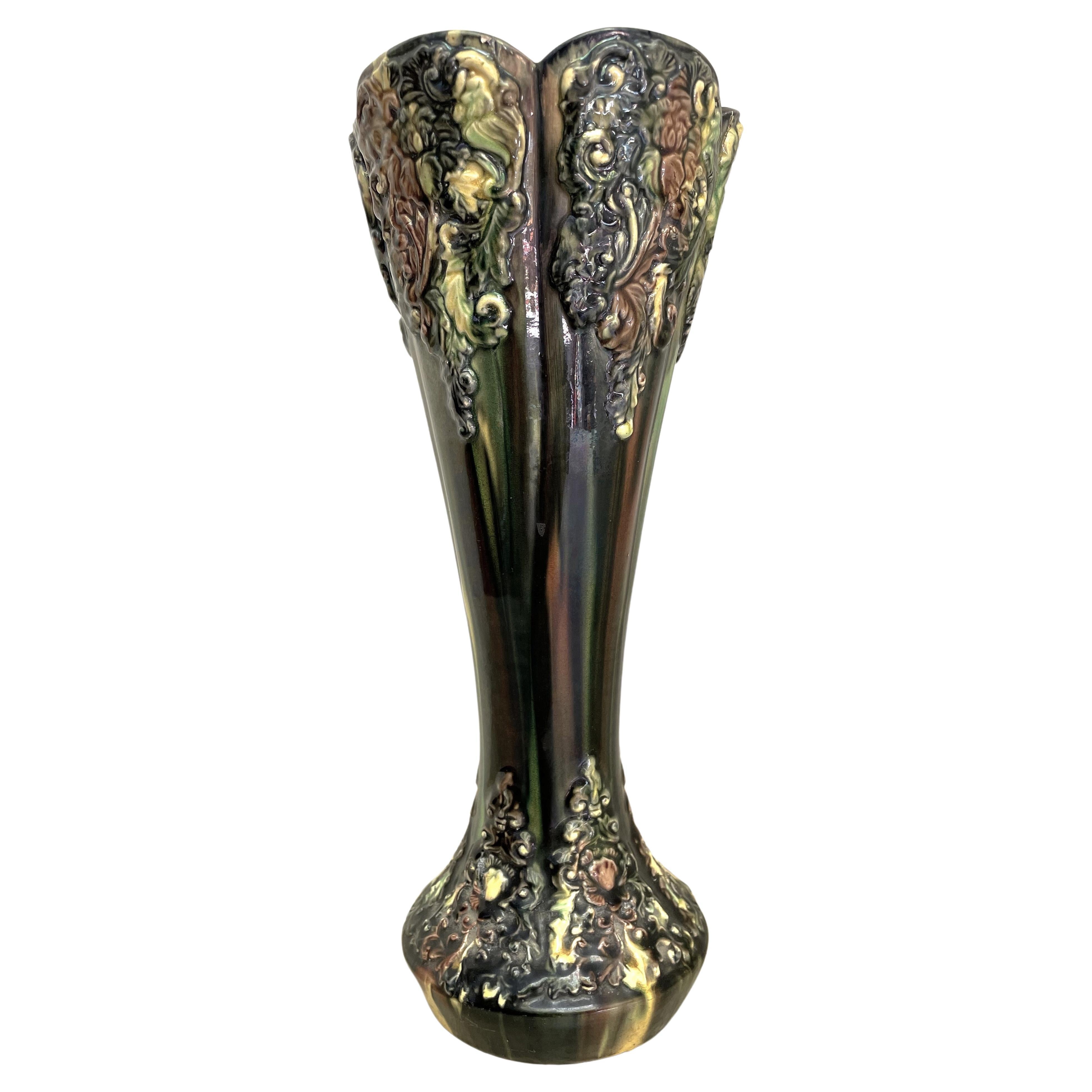 Voici un superbe vase de 12 pouces de haut en majolique avec une superbe combinaison de glaçures vertes, brunes et jaunes. La décoration appliquée est fantastique, avec un mélange de fleurs et de feuilles tourbillonnantes et surchargées. 

Le vase