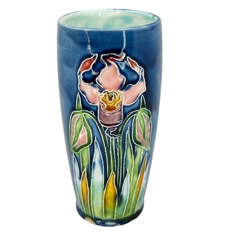 An Art Nouveau majolica ceramic flower motif vase or drinking glass. It is glazed in bright blue, pink, green, and yellow. An Art Deco style orchid takes center stage in the front with blooms and greenery at the bottom. This would be an excellent