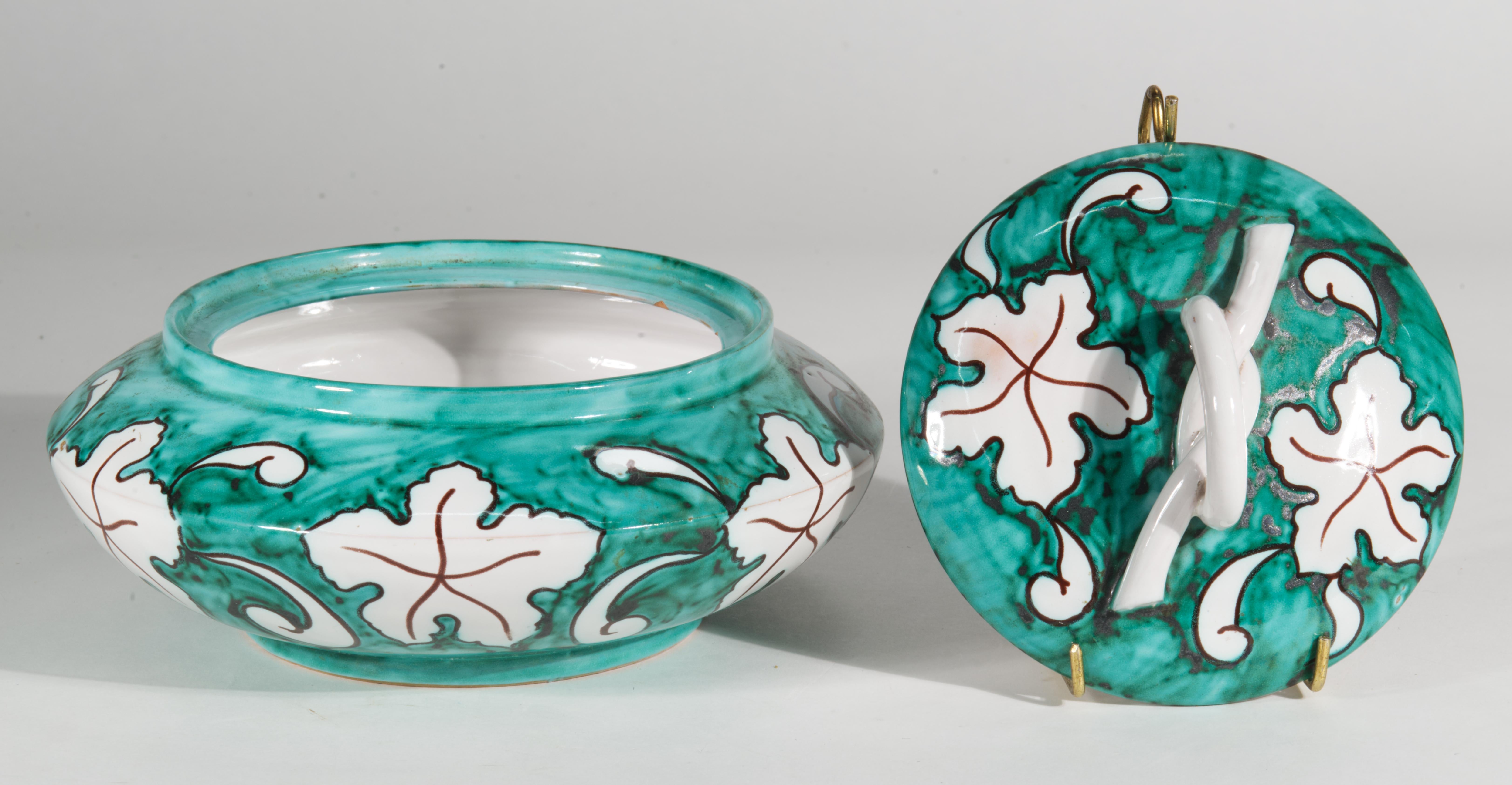 Large round dresser or trinket box with lid features graphic decor with stylized leaves and scrolls motifs on the sides and the lid. The handle is sculpted in shape of a large knot of faux rattan or wicker, reminiscent of Chippendale style pieces.