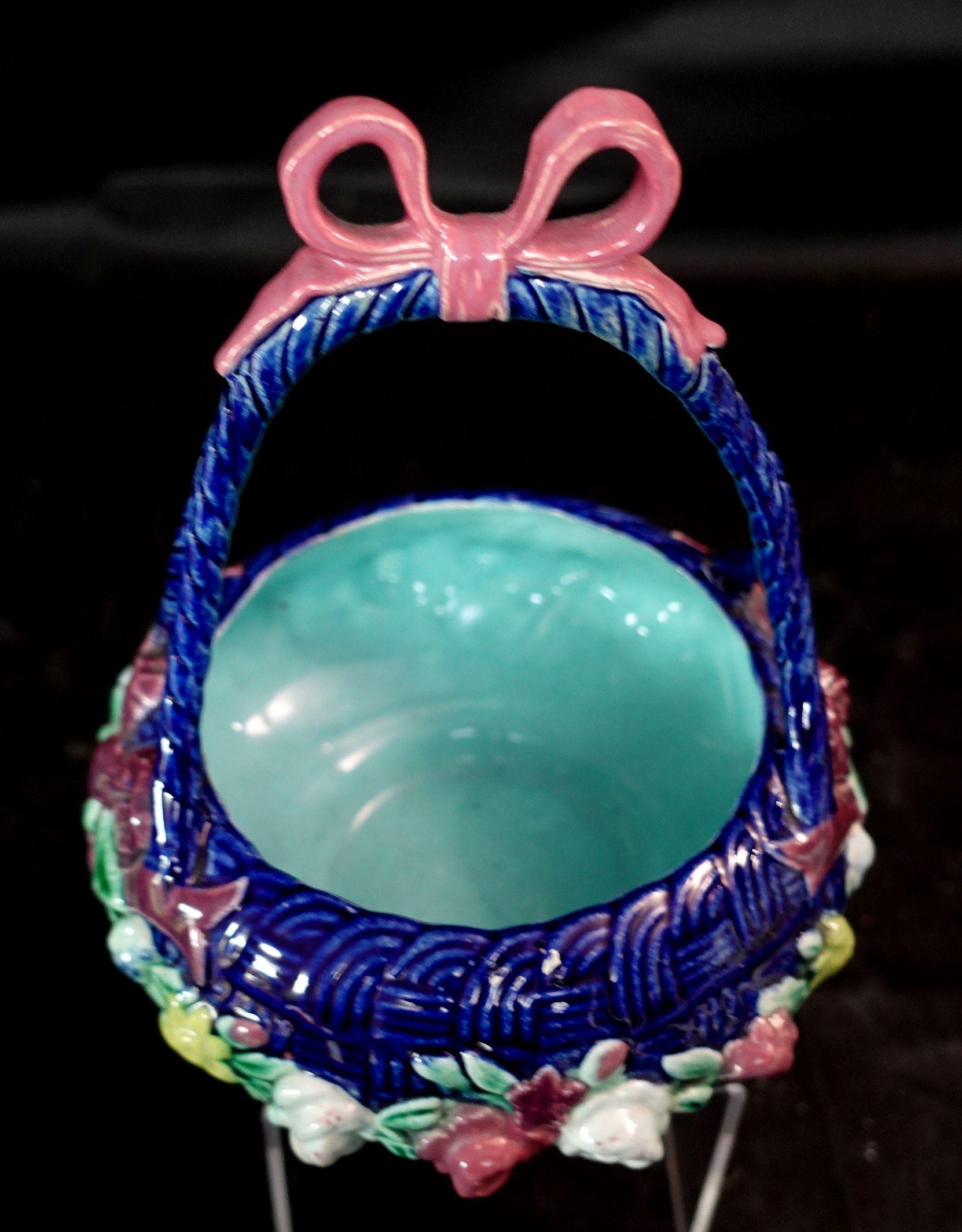 Majolica cobalt ground basket, England, 1870, polychrome enameled and molded with a double strap handle with bow over a circular basketweave ground with a band of raised flowers.