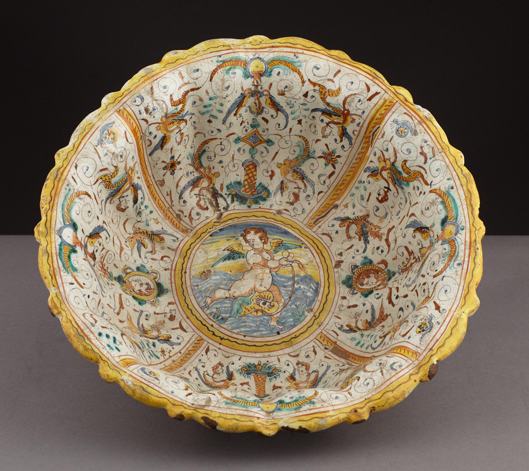 Late 16th-early 17th century comependiario Majolica bowl, Italian, circa 1600-1620.

The white lead glazed deep fluted bowl with compendiario Renaissance decoration, centered on a cherub fishing, with alternating floral panels with birds and