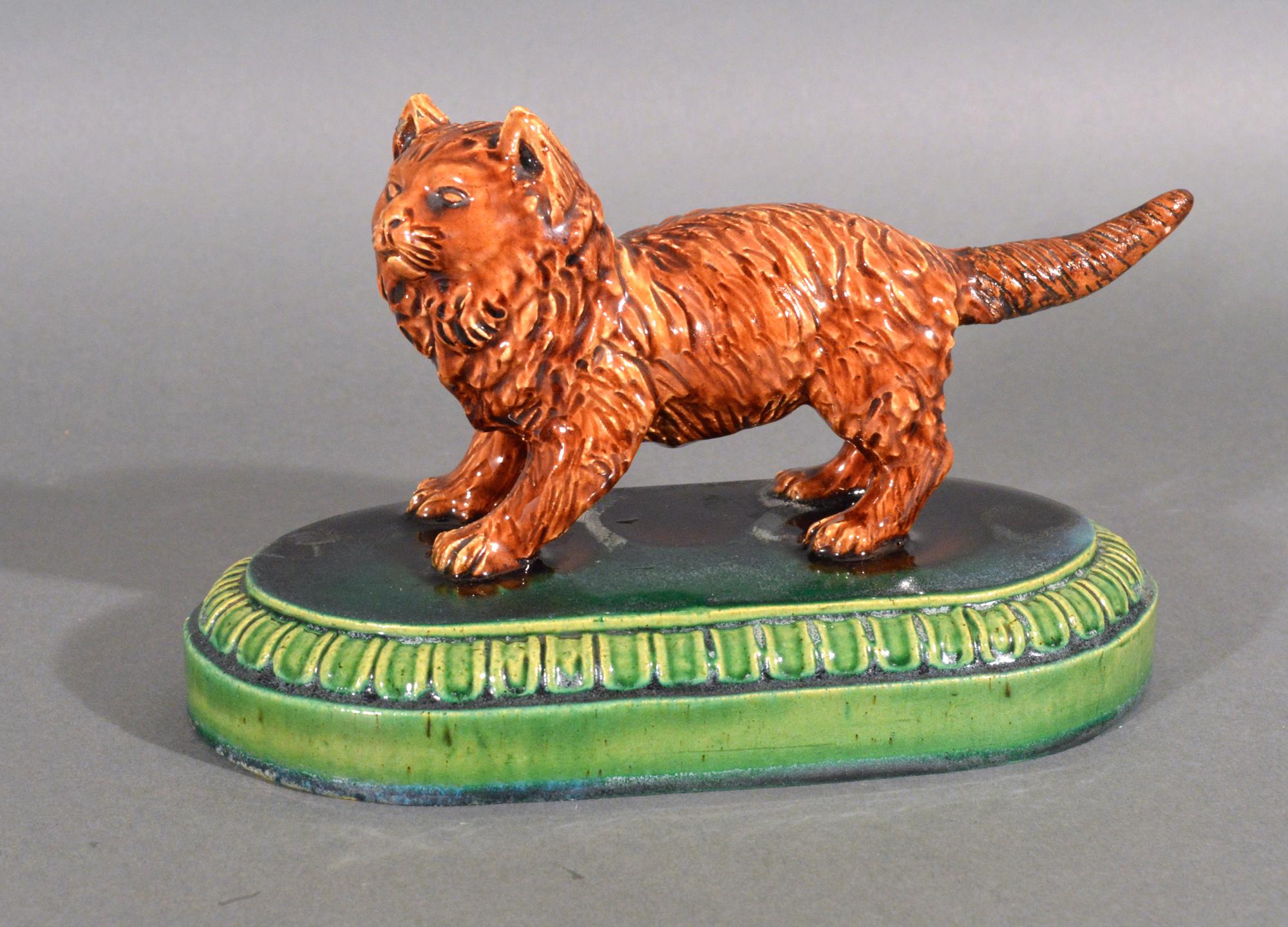 Majolica Model of a Cat,
Earthenware with Majolica Glaze,
Possibly William Brownfield,
19th Century

The figure of a cat is modeled as an orange-brown cat with almost a mane. It is posed as though it is about to pounce with it ears perked and tail